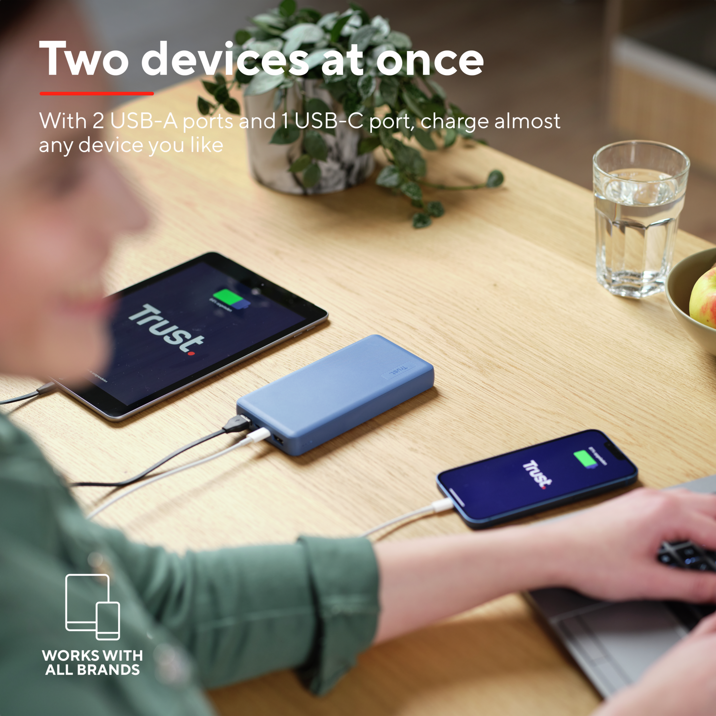 Una batería externa azul carga un smartphone y una tablet en una mesa de madera.