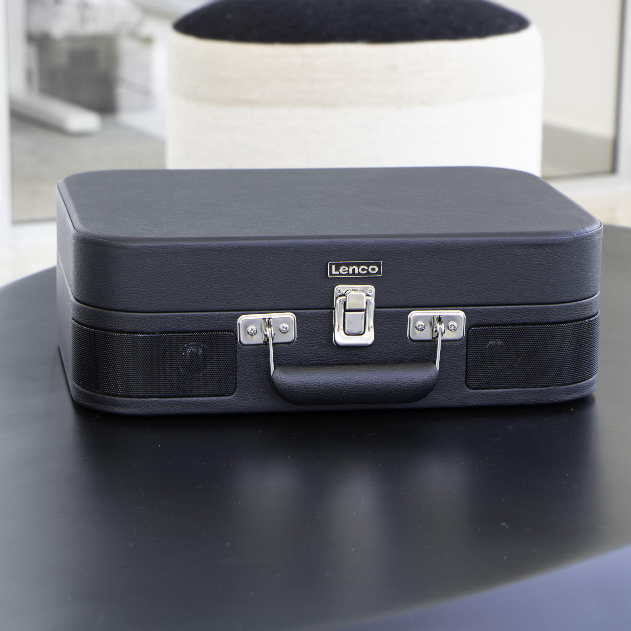 Czarny gramofon walizka ze srebrnymi klamrami i rączką na czarnym stole.