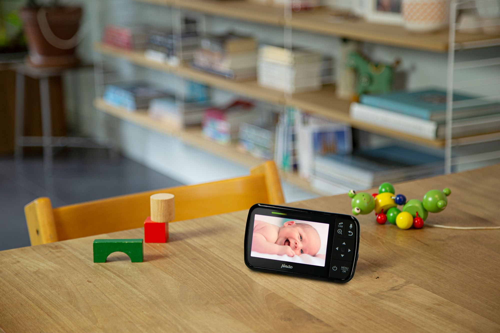 Baby monitor shows sleeping baby, with wooden toys on a table.