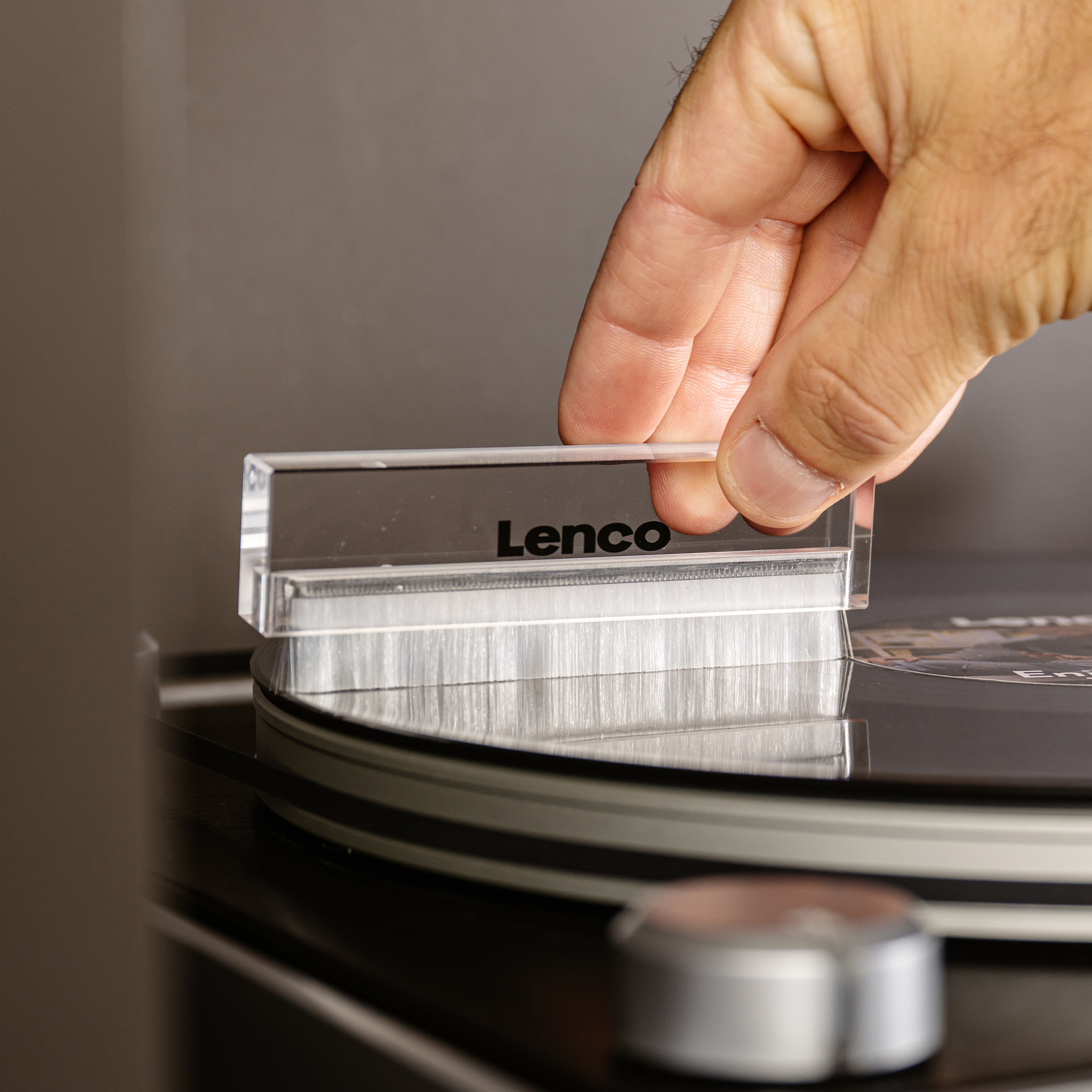 Een hand houdt een Lenco platenspelerborstel boven een vinylplaat.