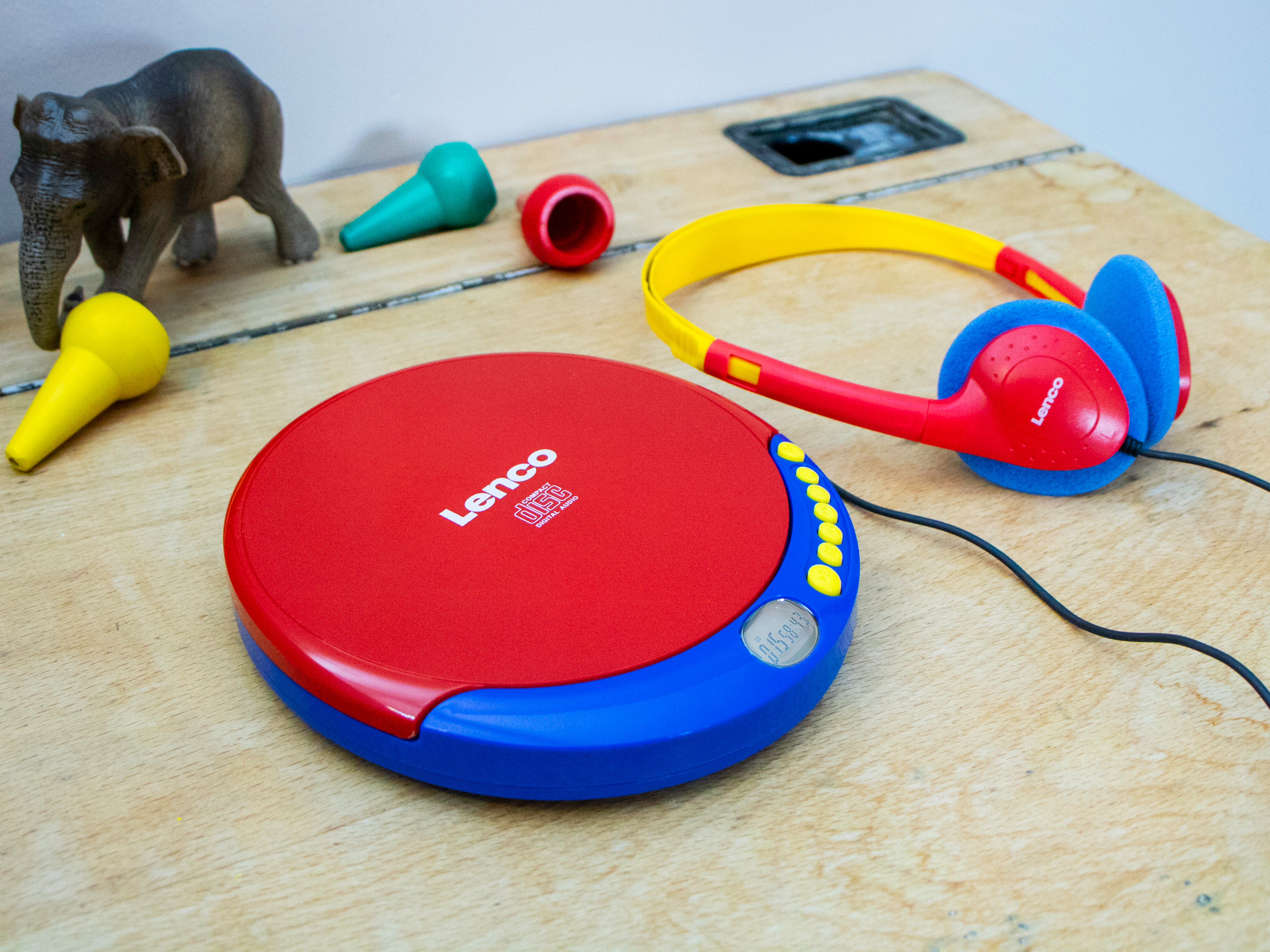 Ein roter und blauer CD-Player mit Kopfhörern und Spielzeug auf einem Holztisch.
