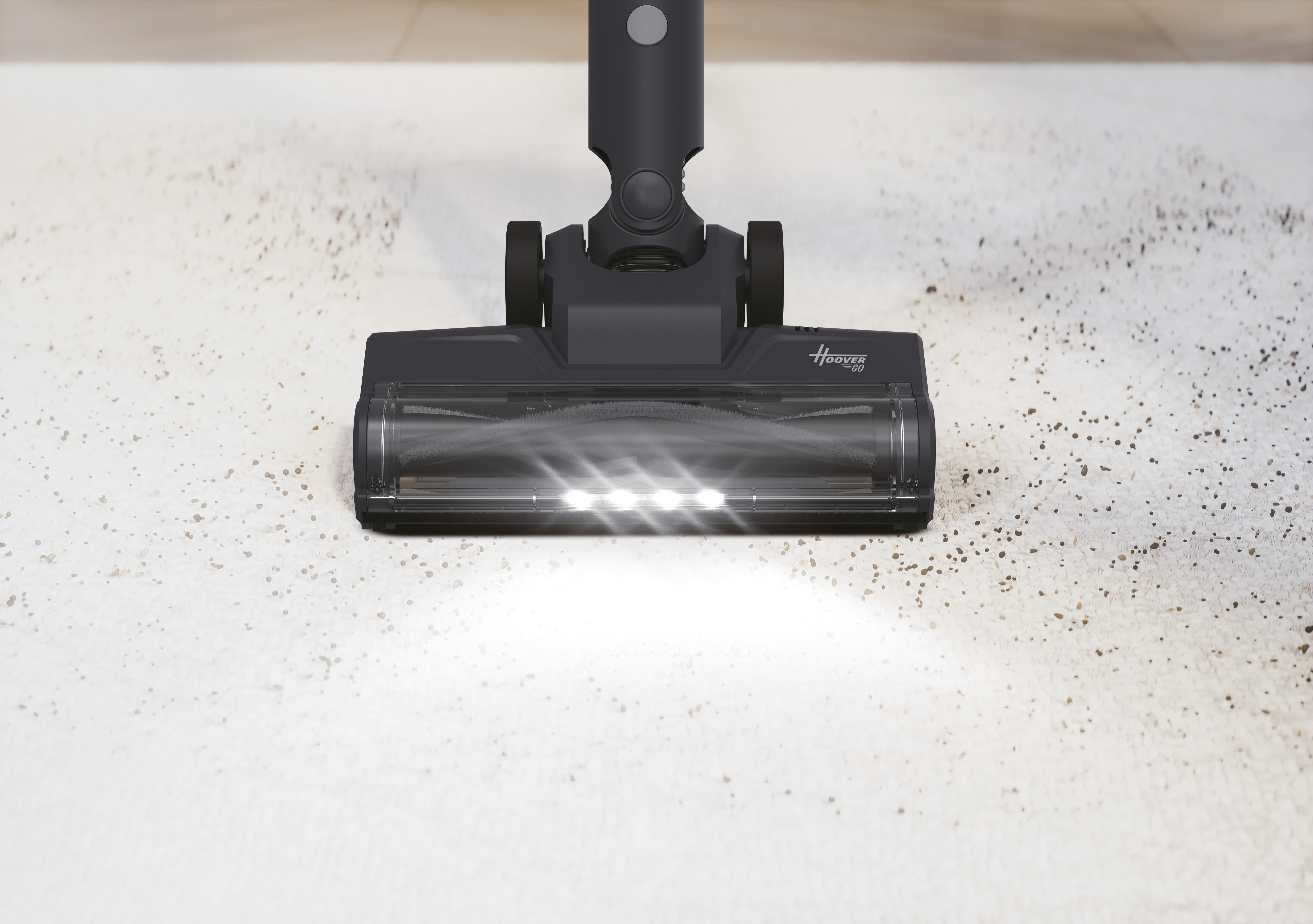 Testata aspirapolvere grigio scuro con luci pulisce un tappeto chiaro con detriti.