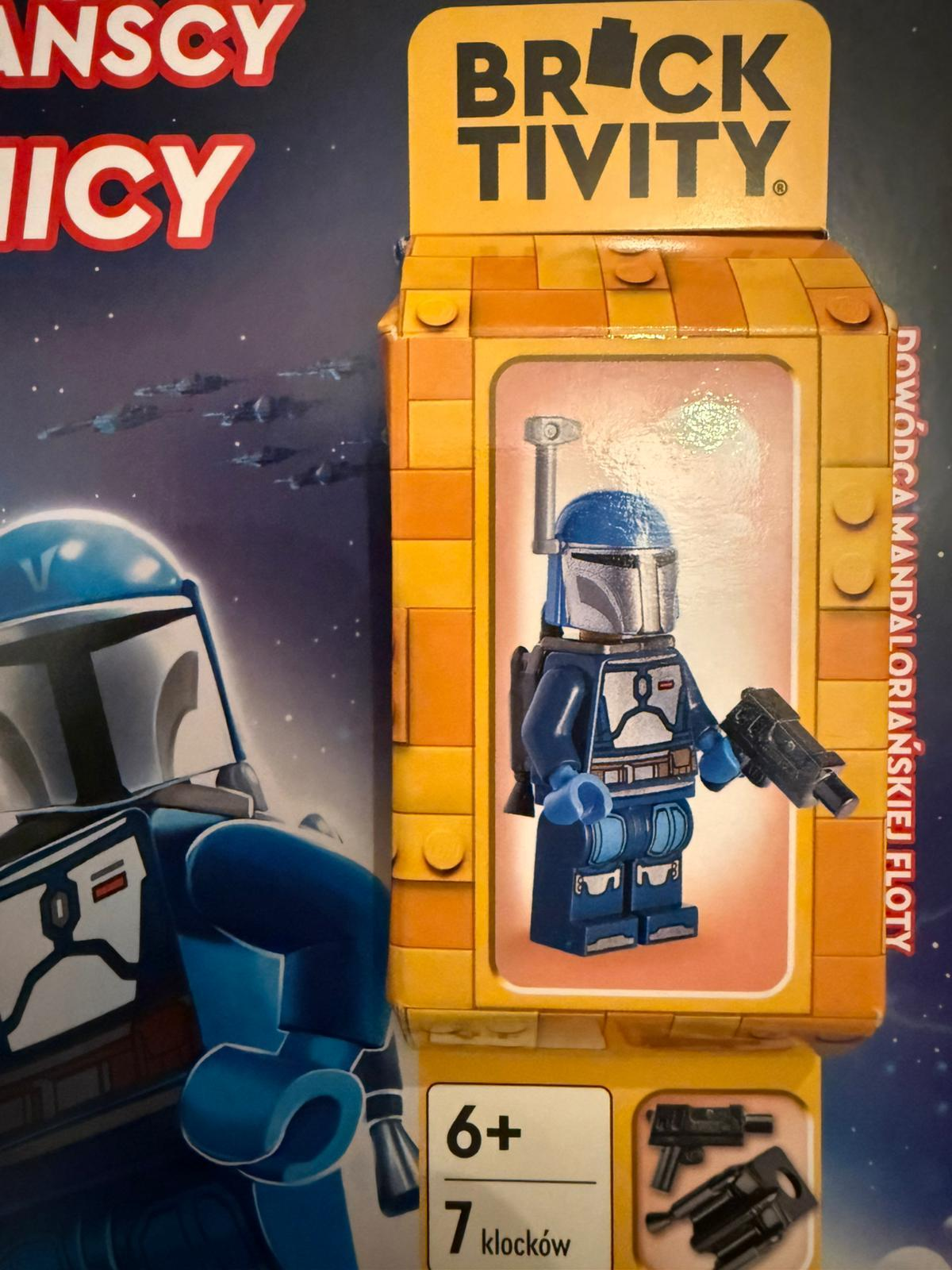Figurka Lego Mandalorian w niebieskiej zbroi z blasterem, na żółtym opakowaniu z klocków.