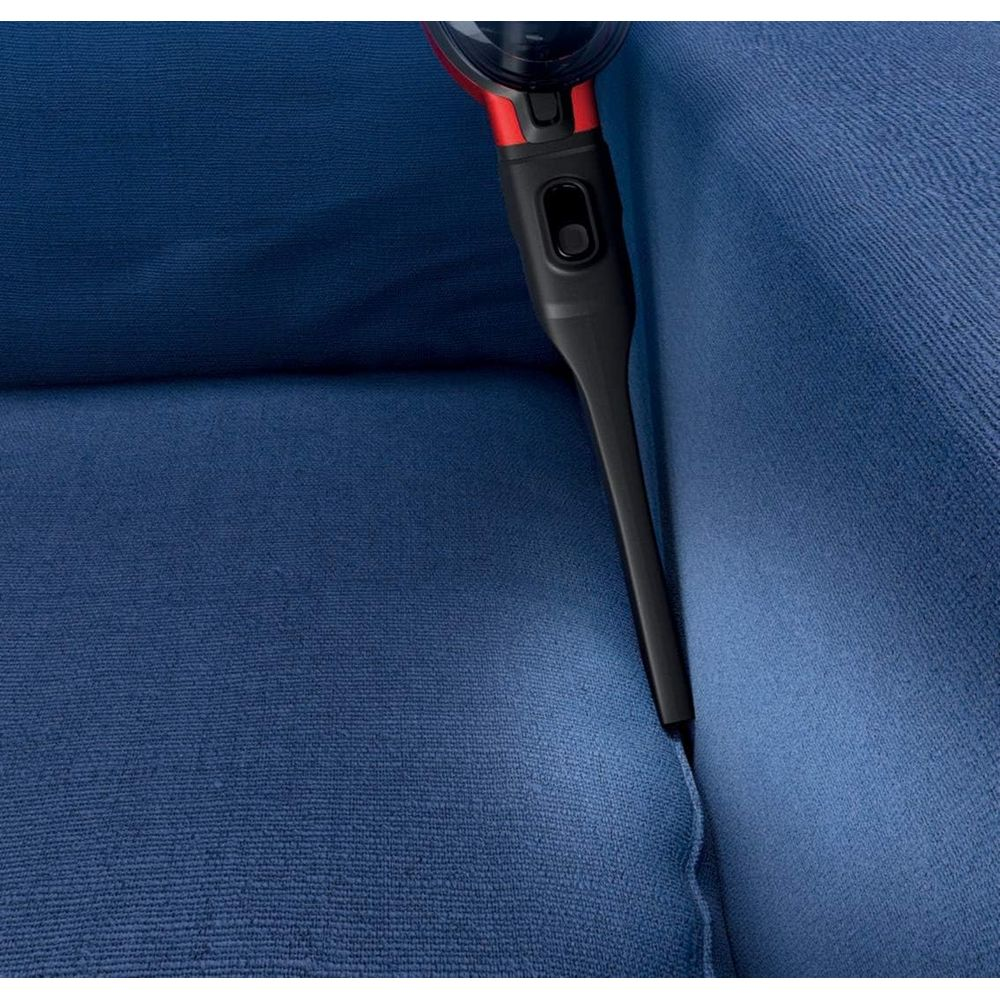 Czarny odkurzacz ręczny z czerwonymi akcentami czyści niebieską kanapę z tkaniny.