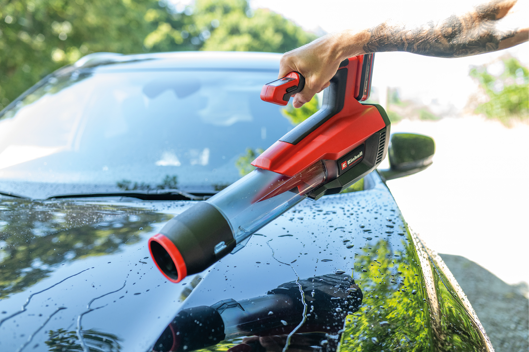 Rote und schwarze Blaspistole trocknet ein nasses schwarzes Auto im Freien.
