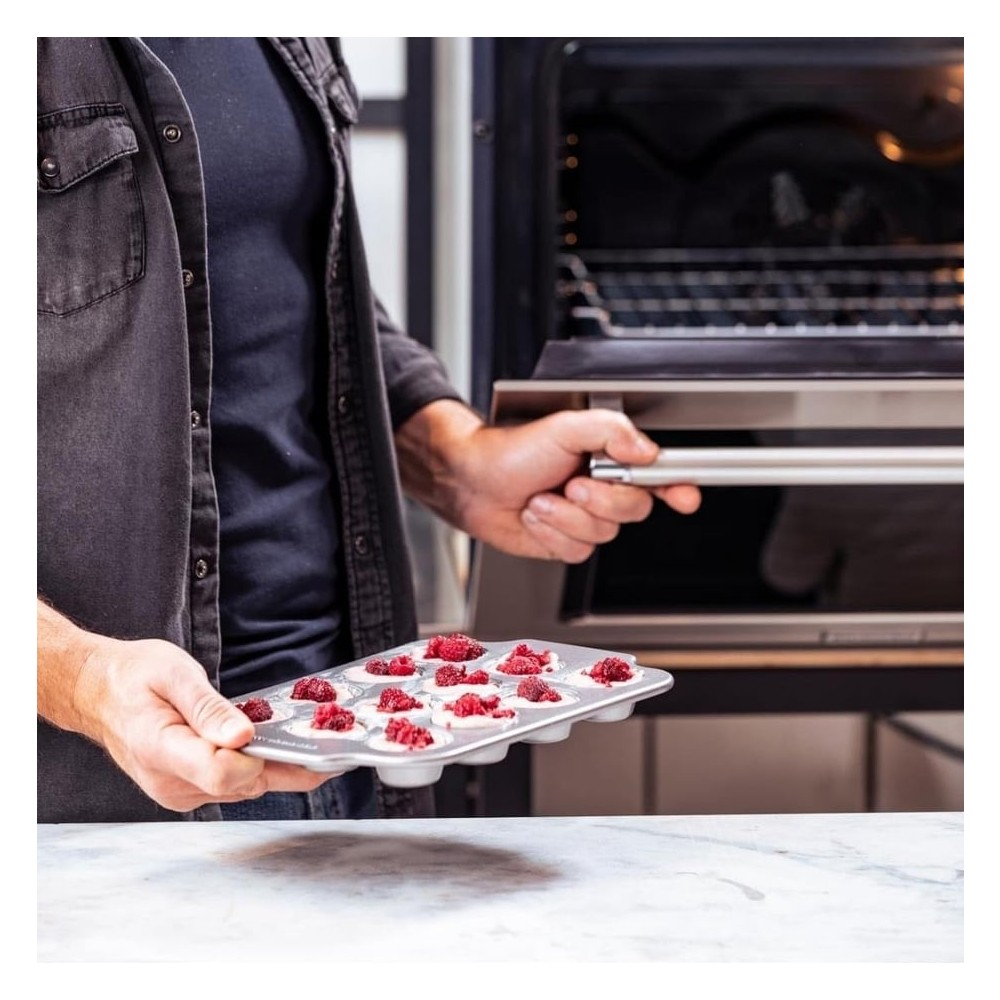 Koyu renk gömlekli bir kişi, frambuazla kaplı pişmemiş kekler içeren bir muffin kalıbı tutuyor.