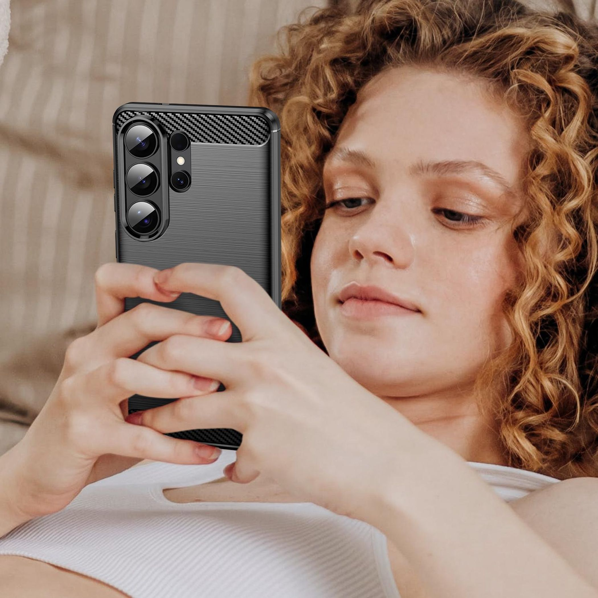 Una mujer con cabello rizado sostiene un teléfono inteligente con funda negra.