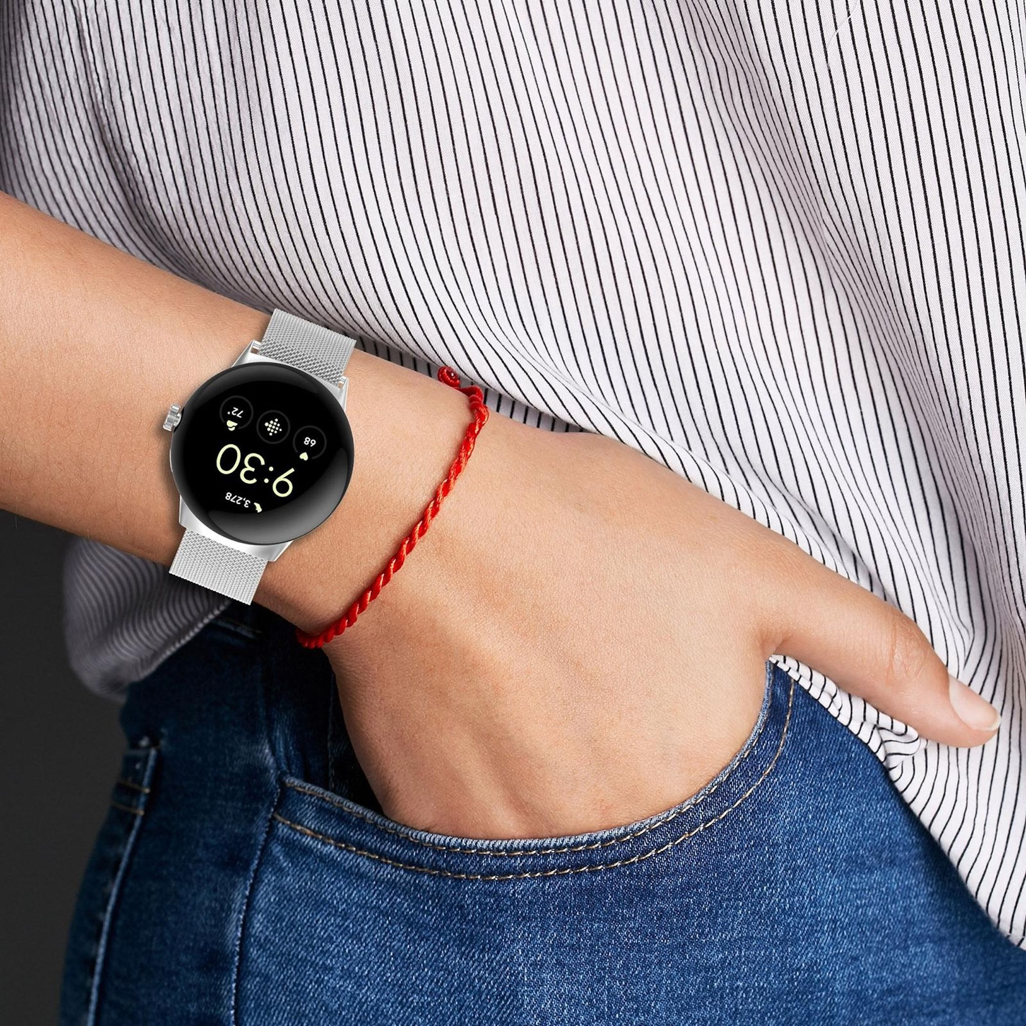 Eine Hand mit einer silbernen Smartwatch und einem roten Band trägt ein gestreiftes Hemd und Jeans.