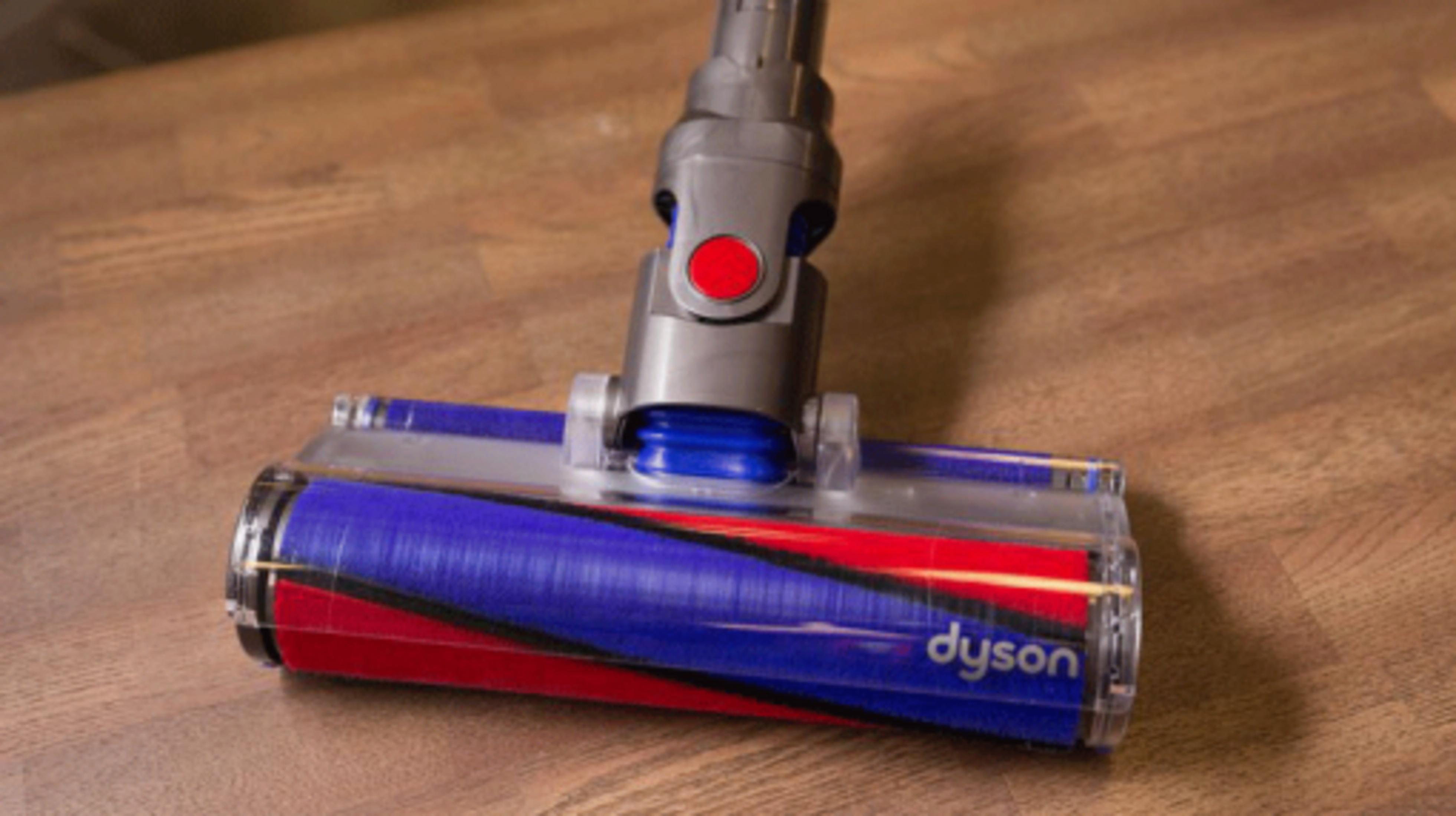Testina aspirapolvere Dyson con spazzola blu e rossa su pavimento in legno.