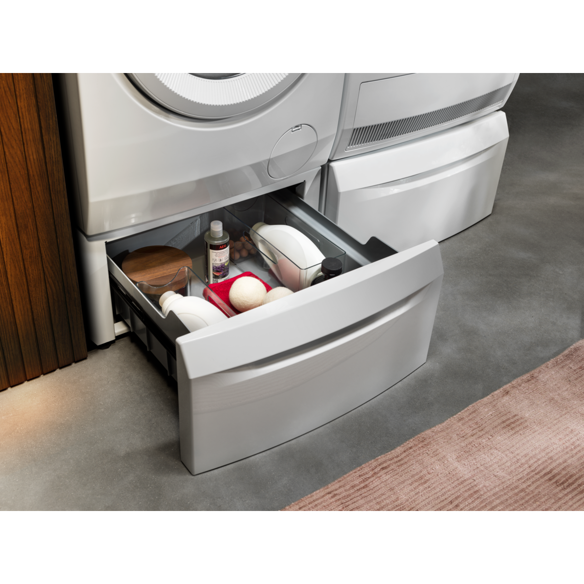 Cassetto aperto di una base lavatrice con detersivo, palline e tagliere in legno.