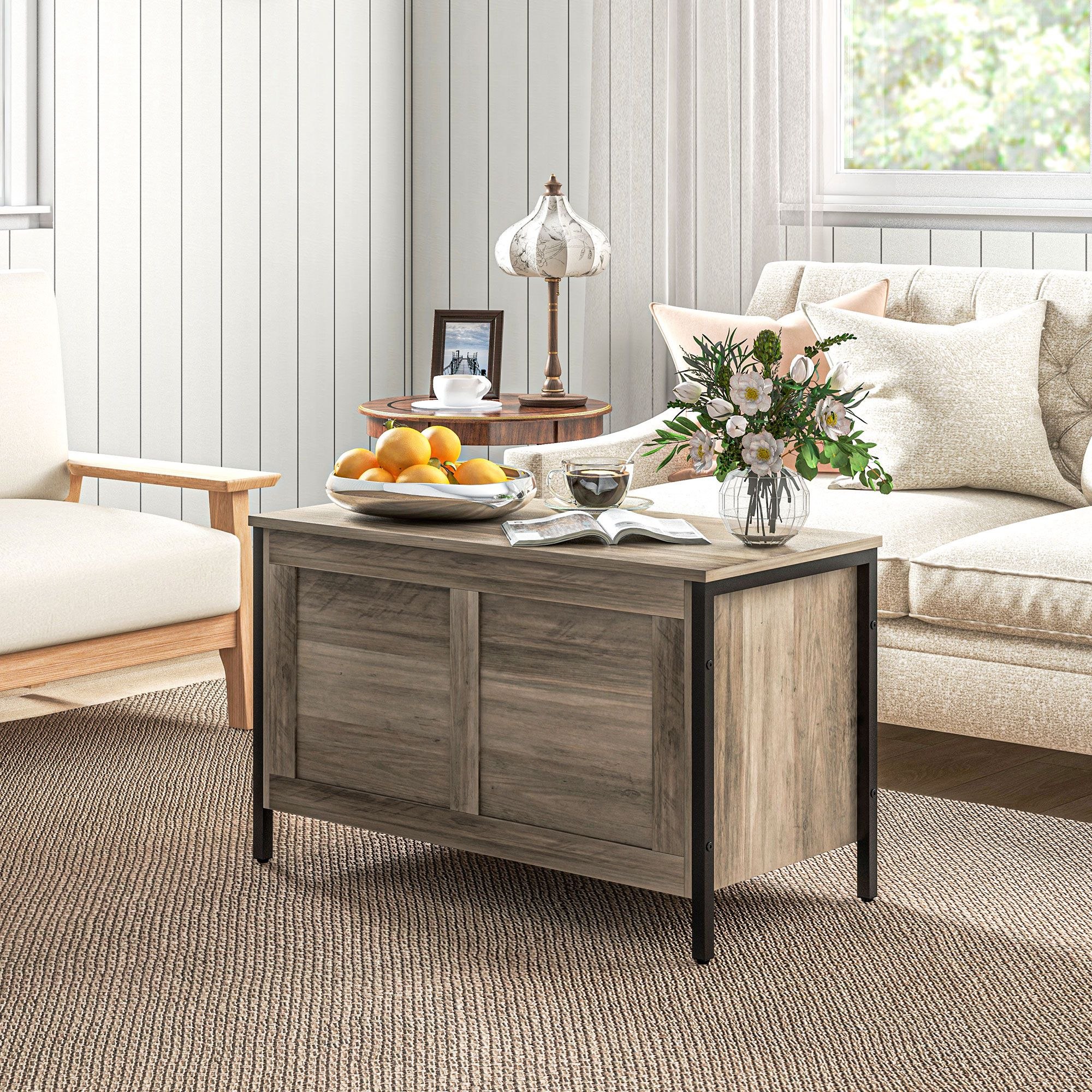 Una sala de estar con baúl de madera, sofá, sillón, lámpara, frutero y flores.