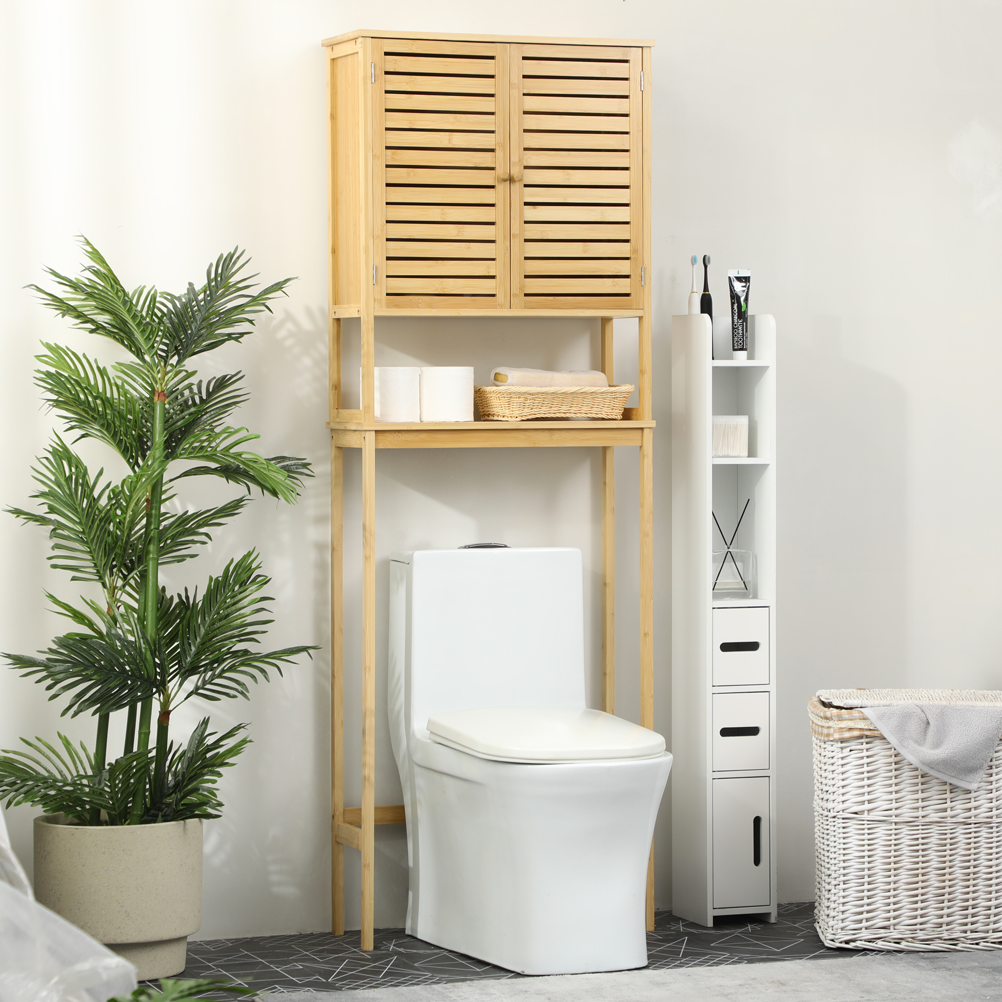 Baño con estante de bambú sobre inodoro, planta, armario blanco y cesto de ropa.