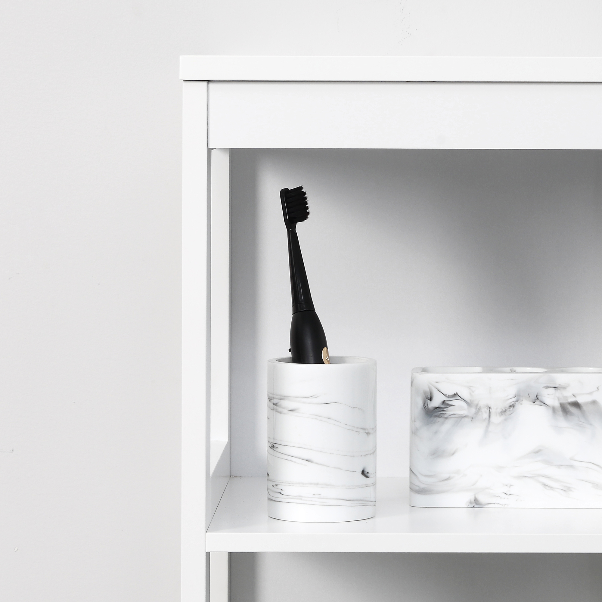 Un cabezal de cepillo de dientes eléctrico negro está en una taza de mármol en un estante blanco.