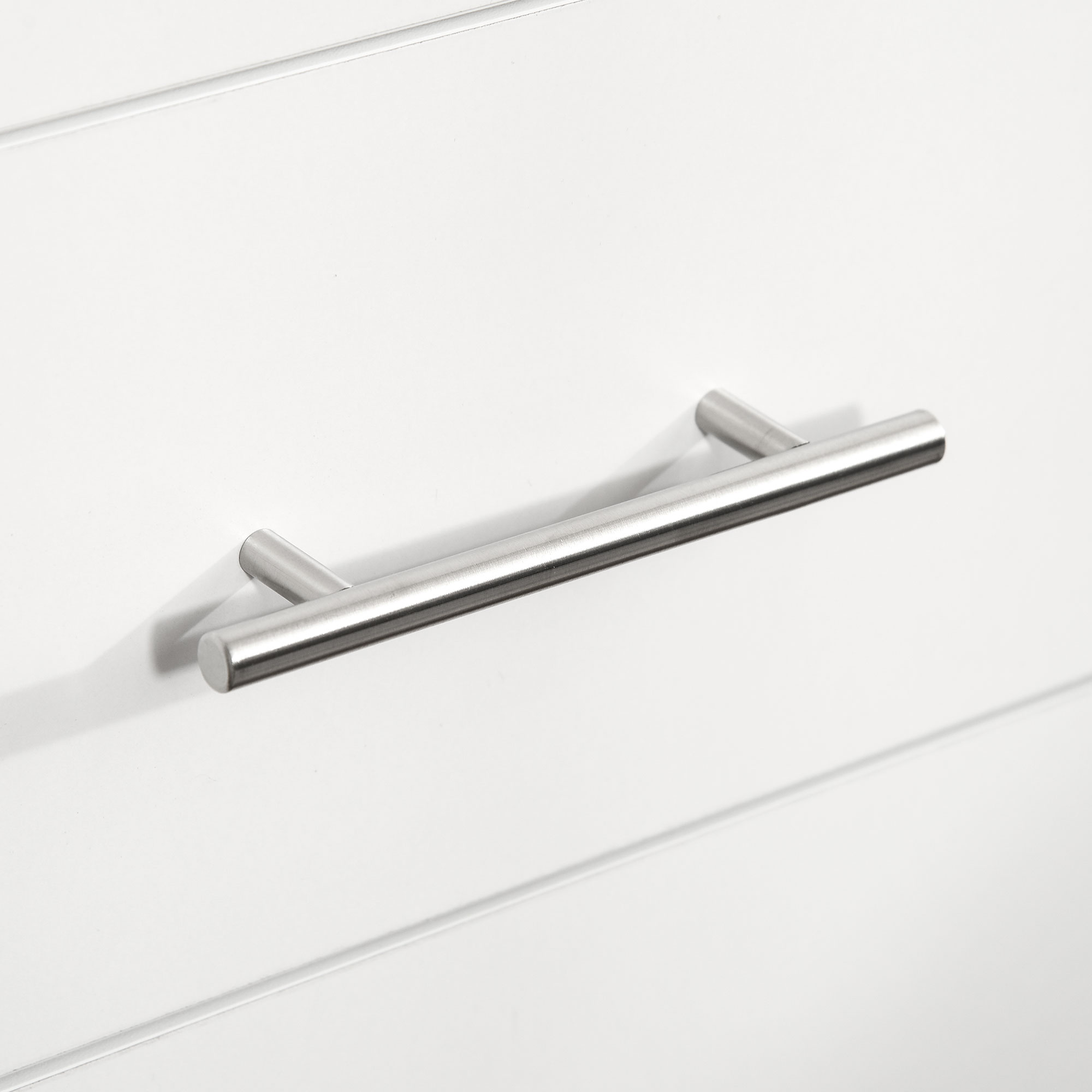 Un tirador de mueble plateado sobre superficie blanca con líneas horizontales.