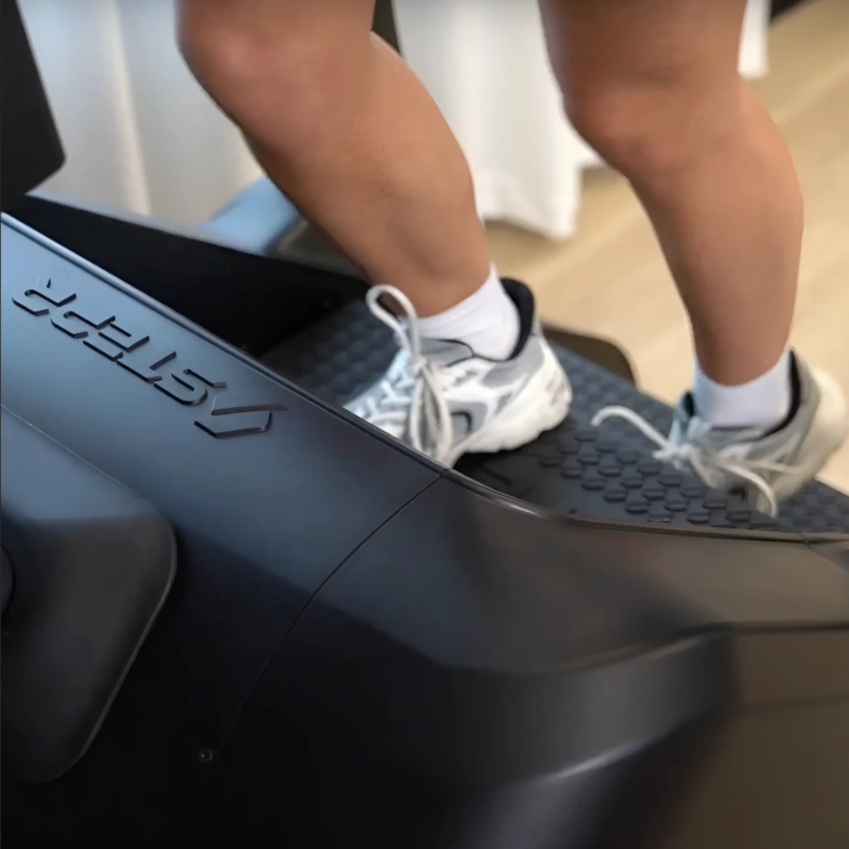 Legs in white socks and sneakers on a black stepper machine with a logo.