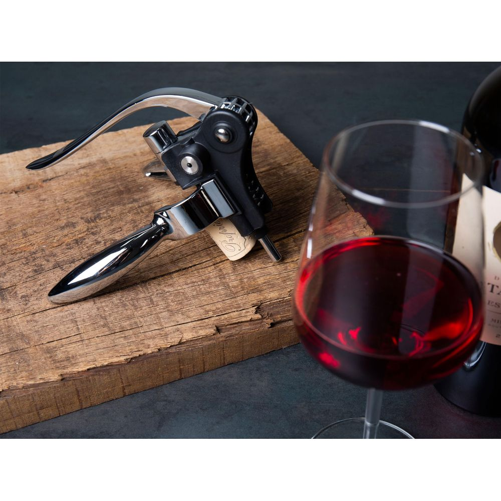 Ein Weinöffner liegt auf Holz neben einem Glas Rotwein.