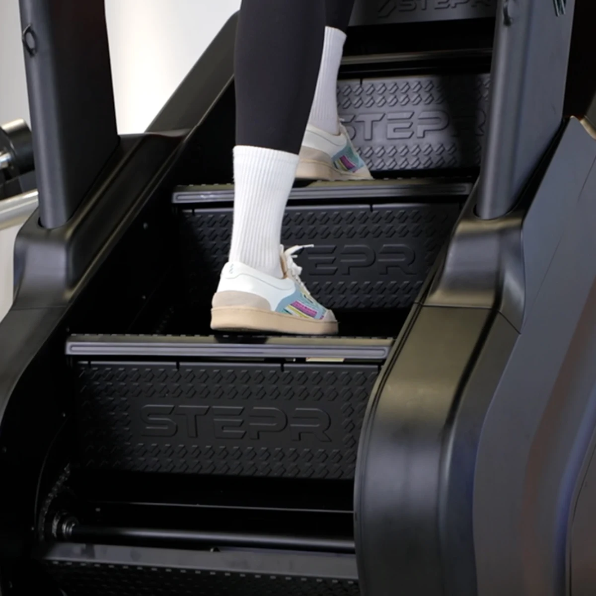 Person in white socks and colorful sneakers climbs black stairs.