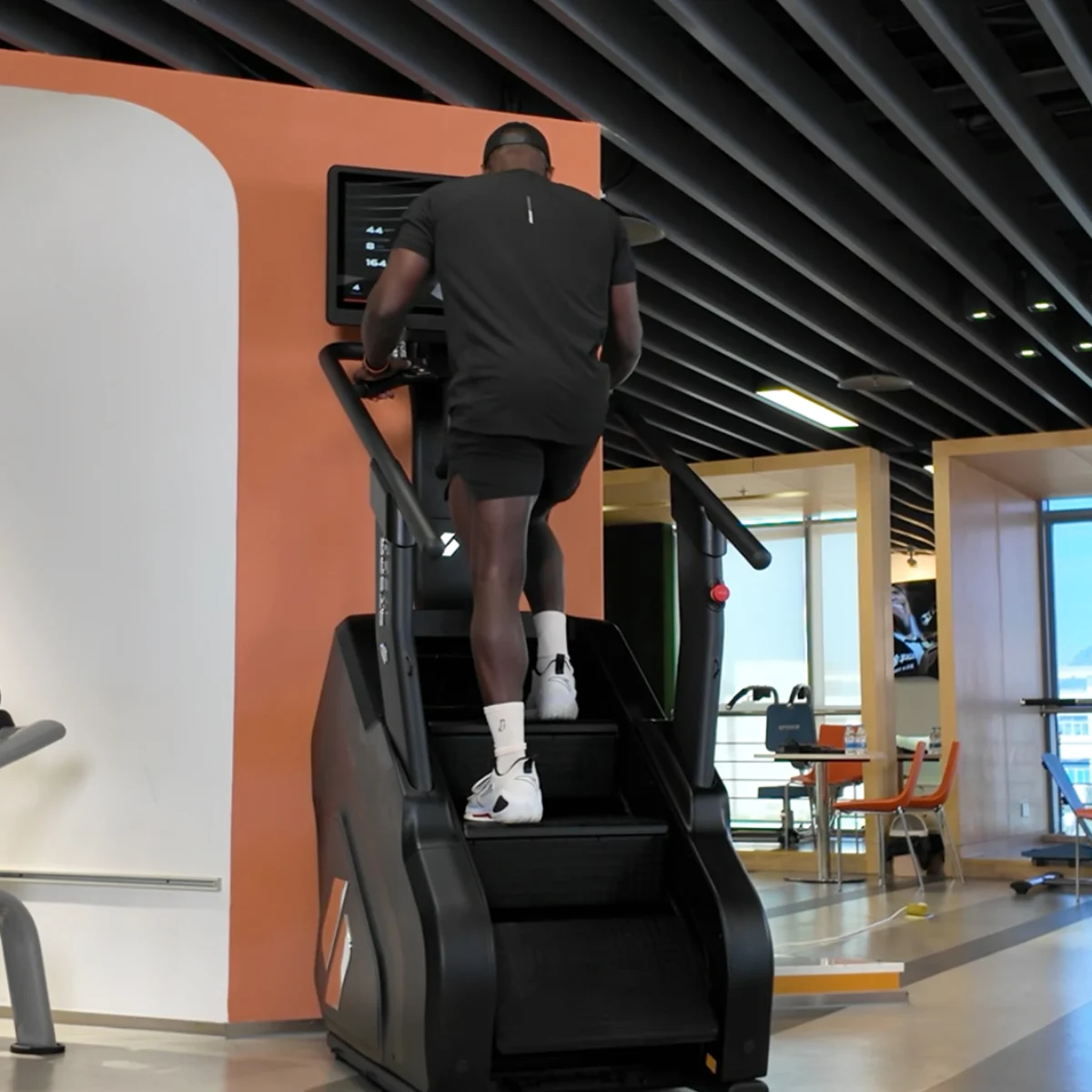 A man in black exercises on a stair climber in a gym.