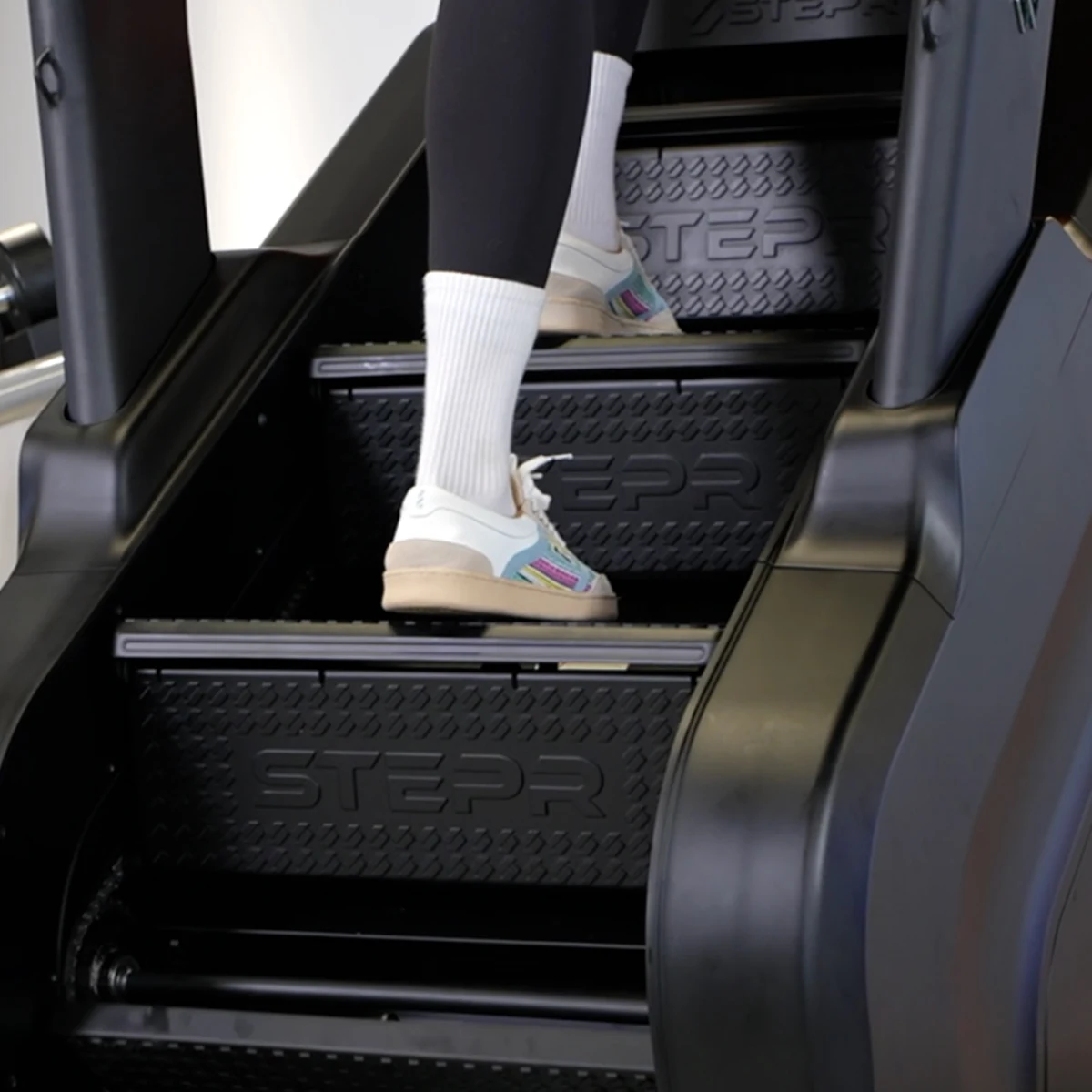 Person in black leggings, white socks, and colorful sneakers climbing black stairs.