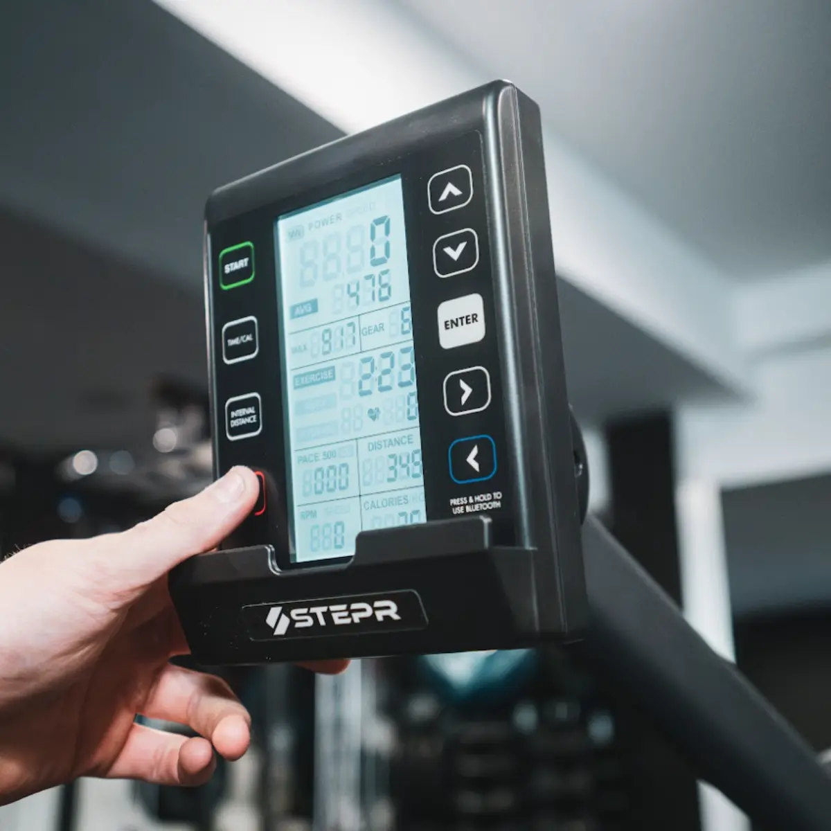 Close-up van een fitnessapparaatdisplay met een hand die op een knop drukt.