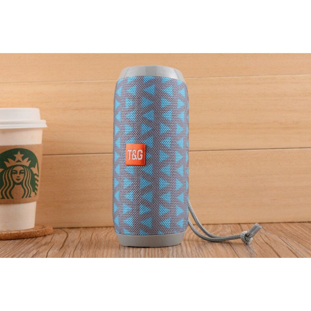 Grauer Lautsprecher mit blauem Muster, neben einer Kaffeetasse auf Holzhintergrund.