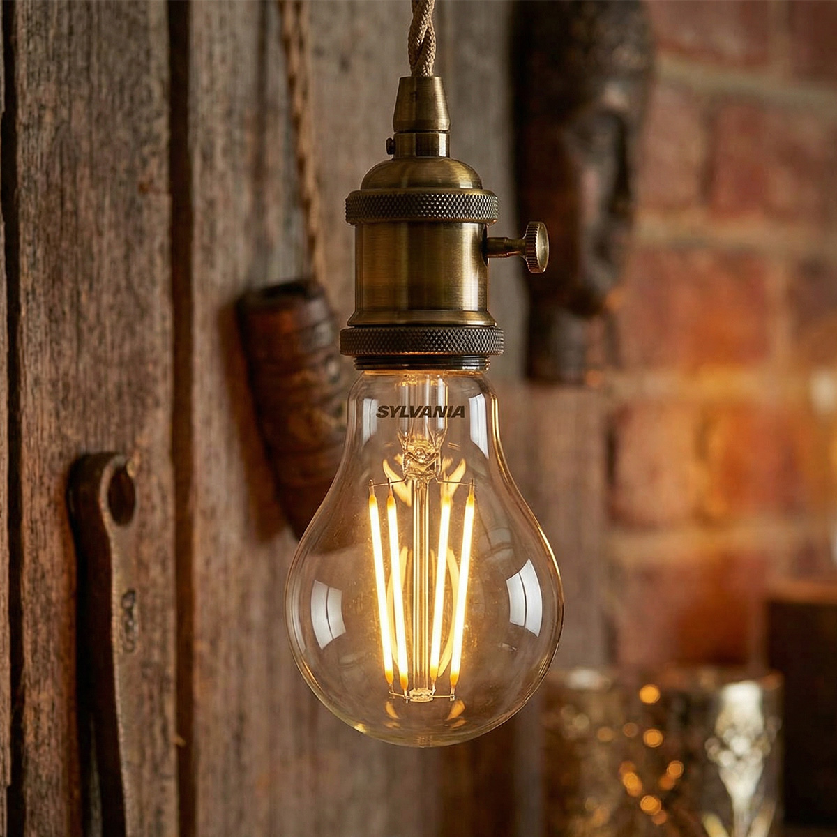 Une ampoule Edison à douille en laiton pend devant un mur en bois.