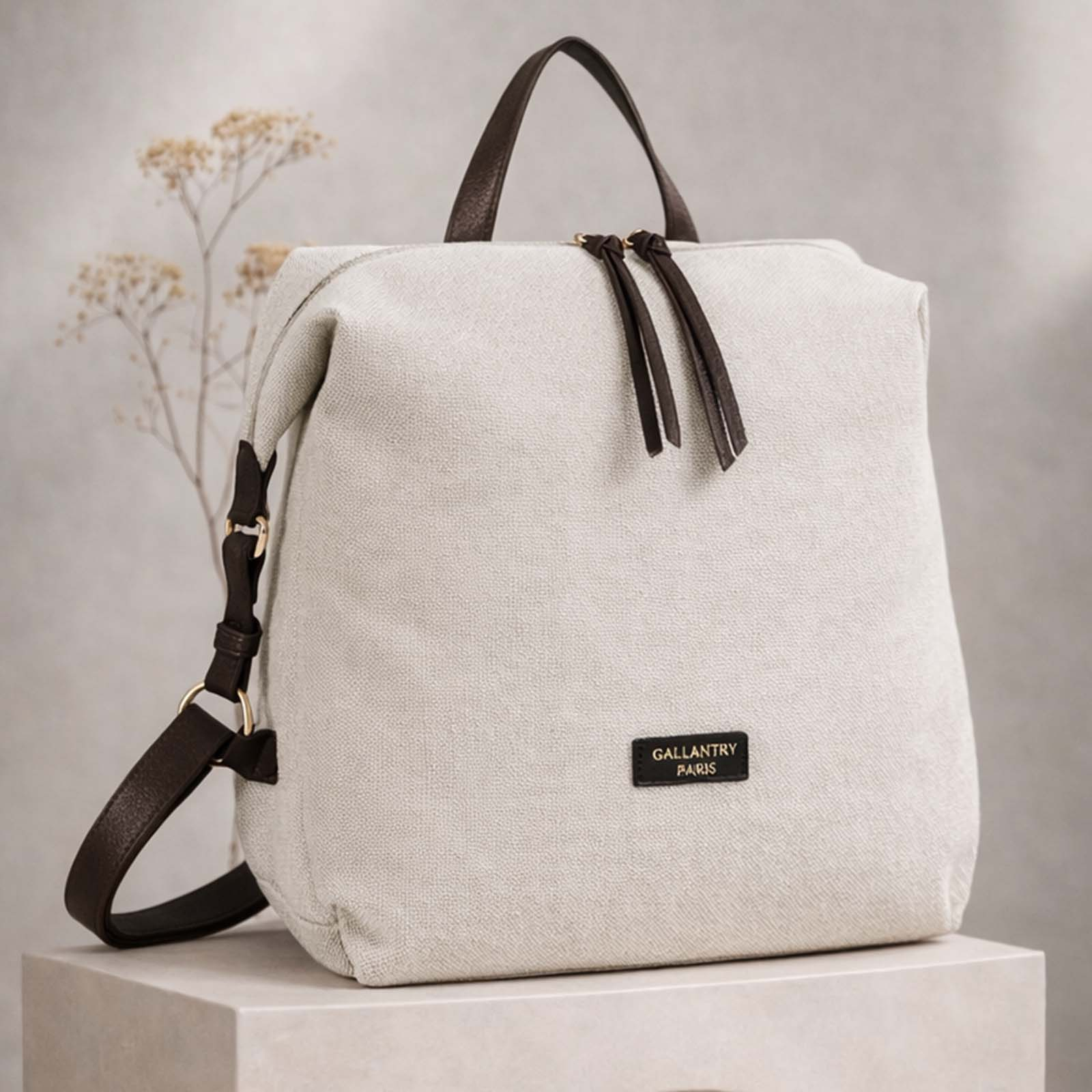 Ein beigefarbener Rucksack aus Stoff mit braunen Lederdetails steht auf einem Podest.