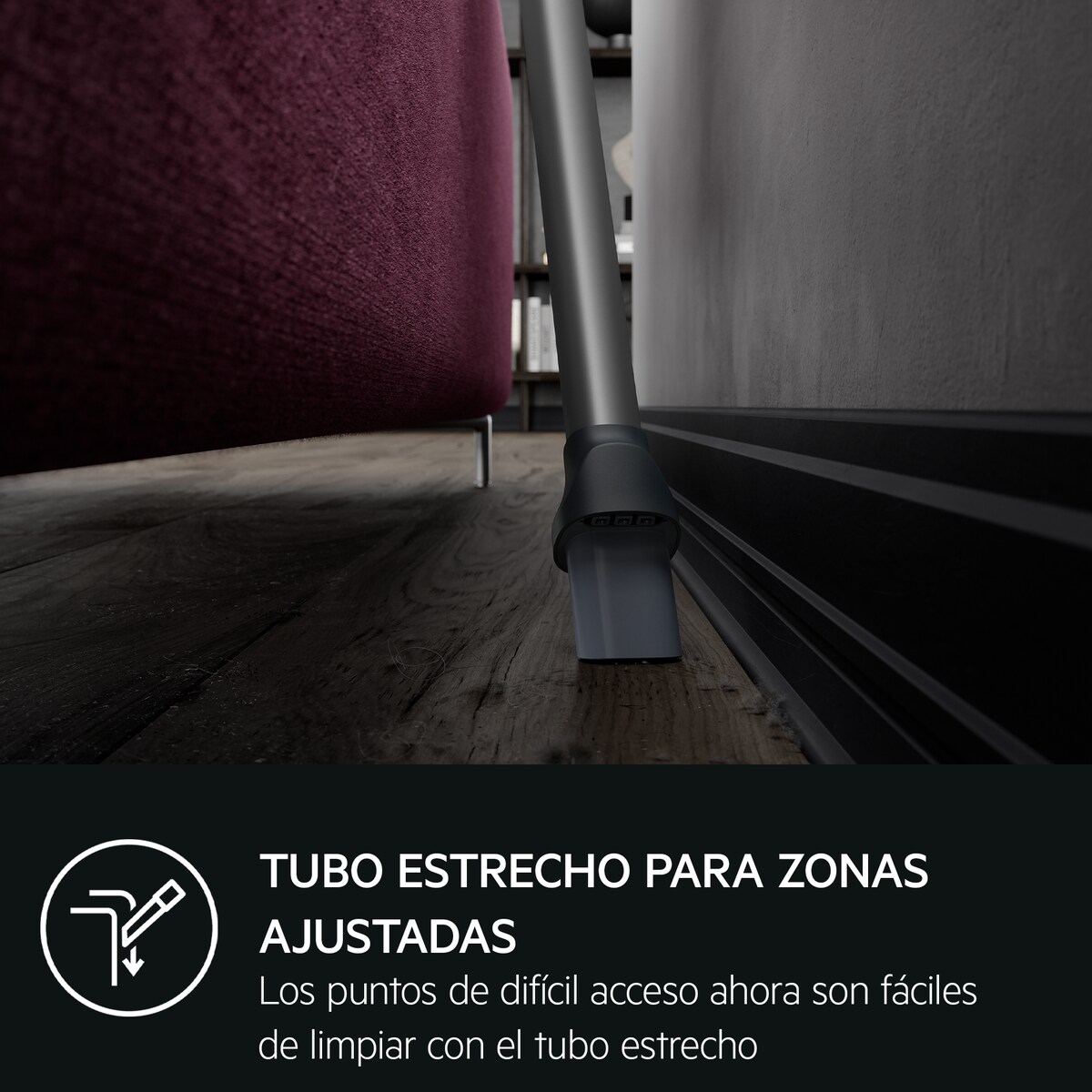 Un accesorio estrecho de aspiradora limpia bajo un sofá morado y junto a una pared.