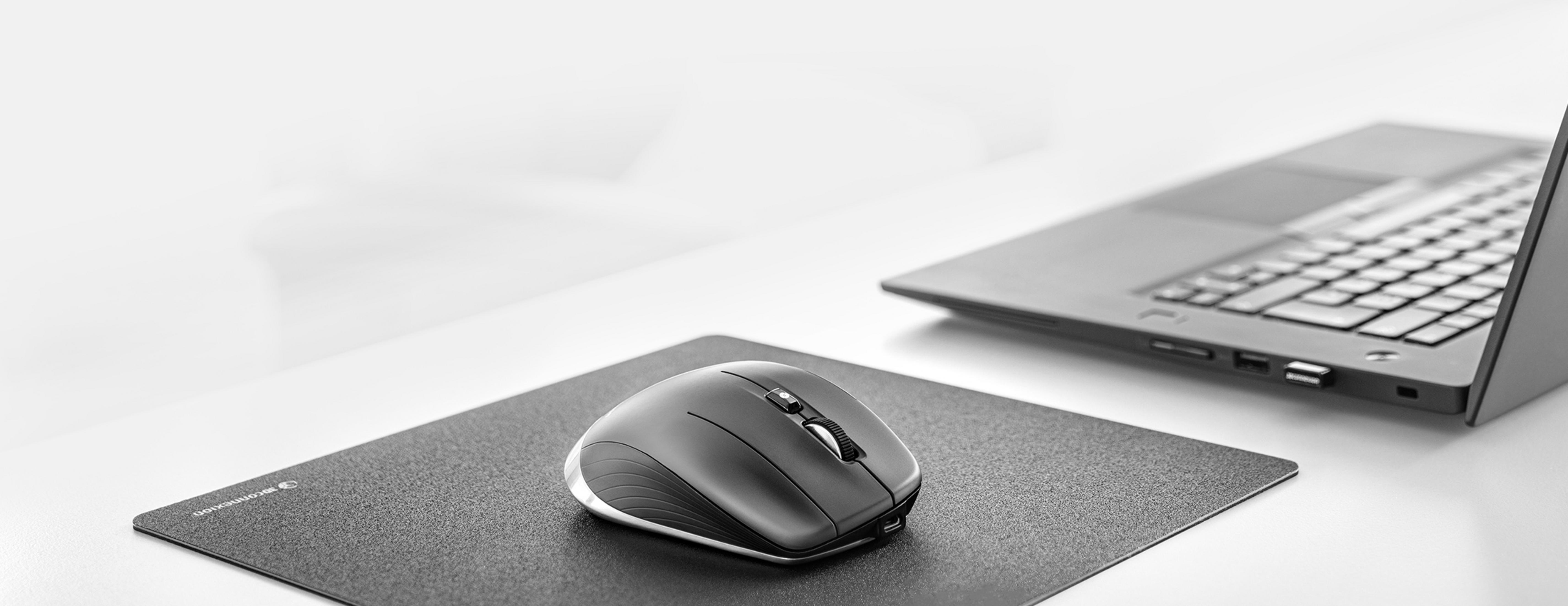 Eine schwarze Maus liegt auf einer schwarzen Unterlage neben einem Laptop.
