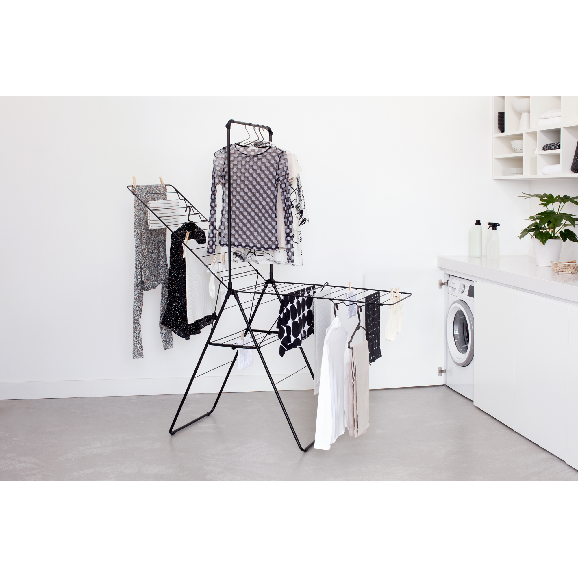 A black drying rack with clothes, a washing machine next to it.