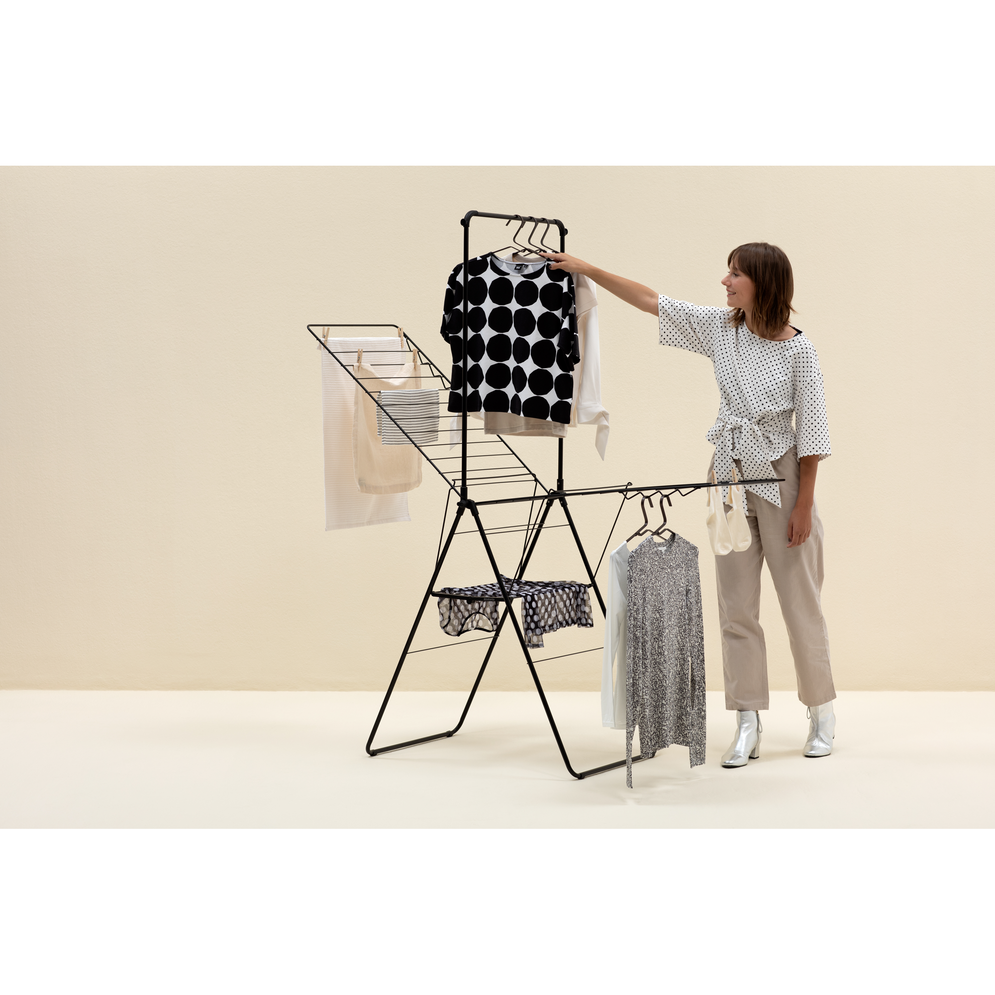 Woman in polka dot blouse hangs clothes on a black drying rack.