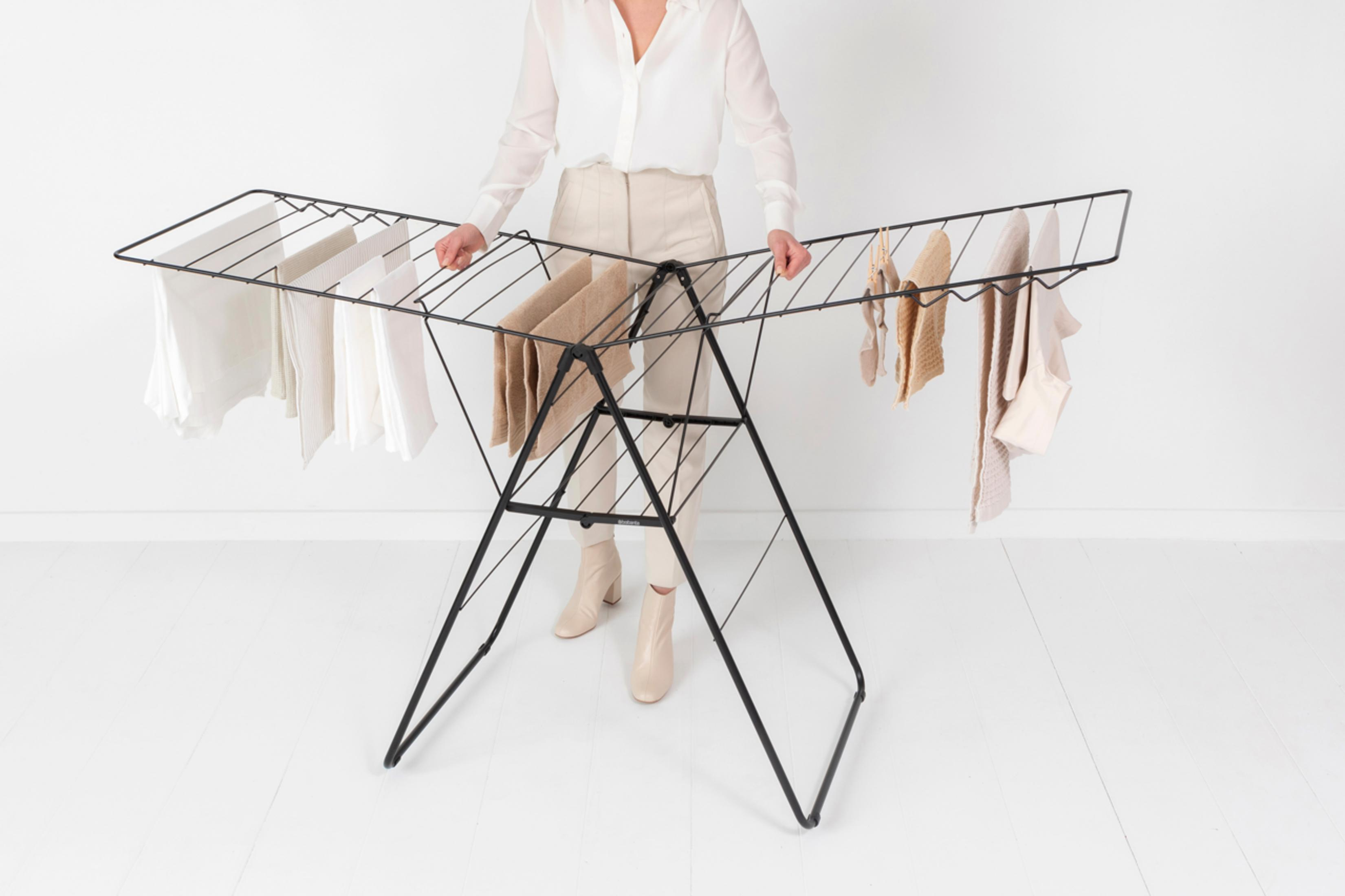 A person stands next to a black drying rack with white and beige clothes.