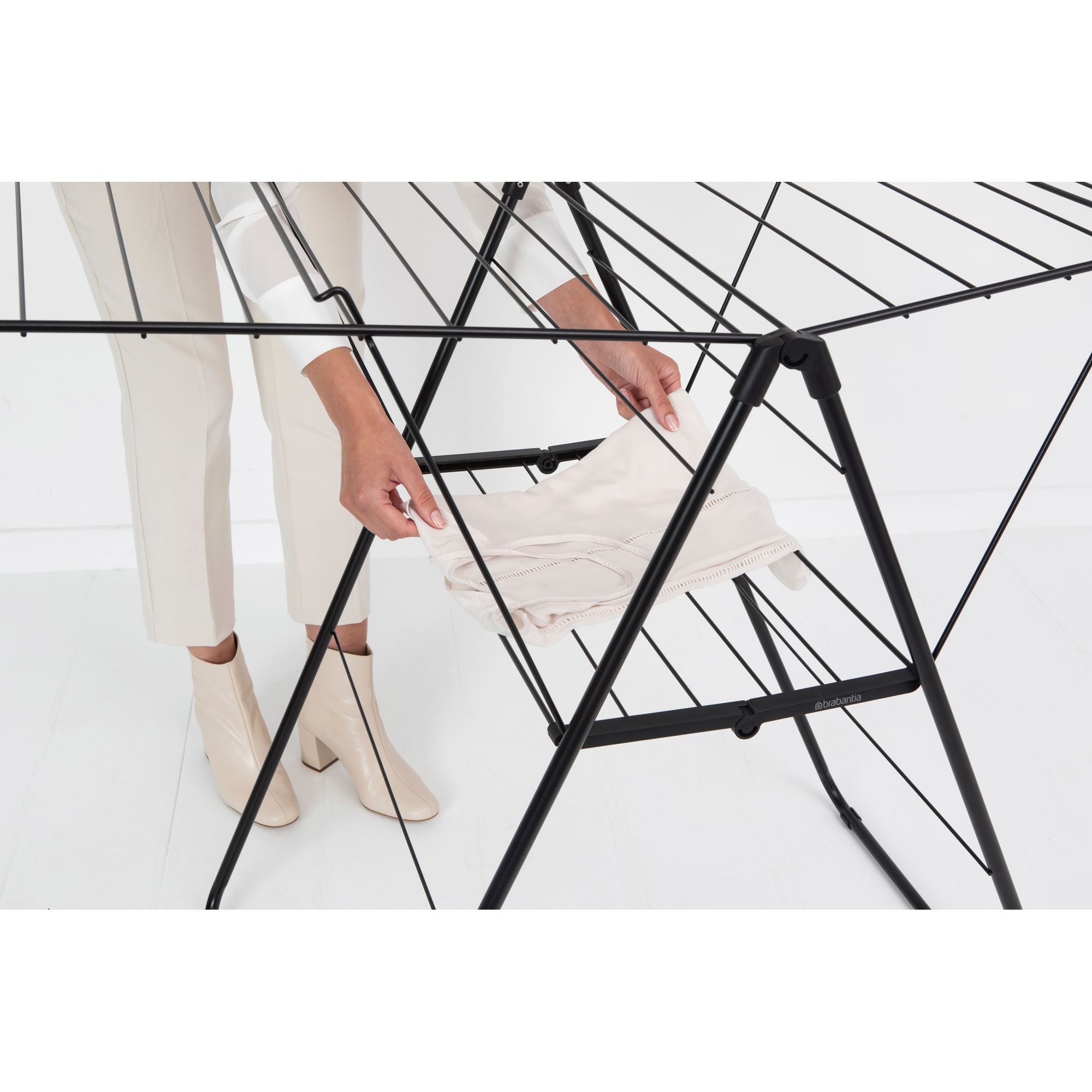 A person places a light-colored garment on a black drying rack.