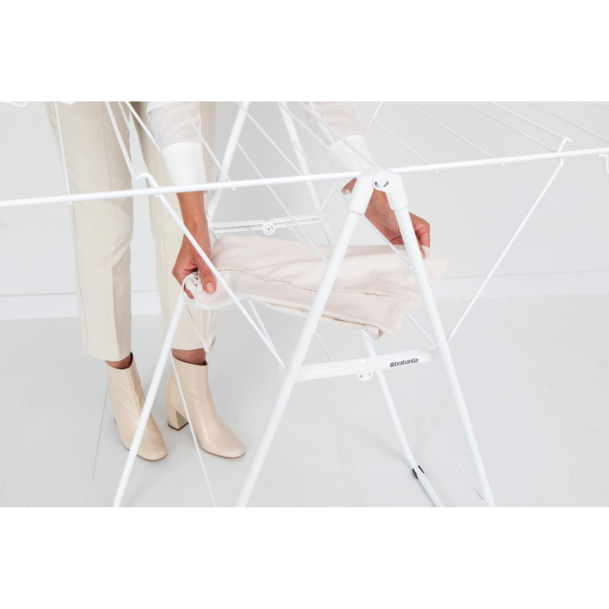 A person is folding a light-colored sheet on a white drying rack.