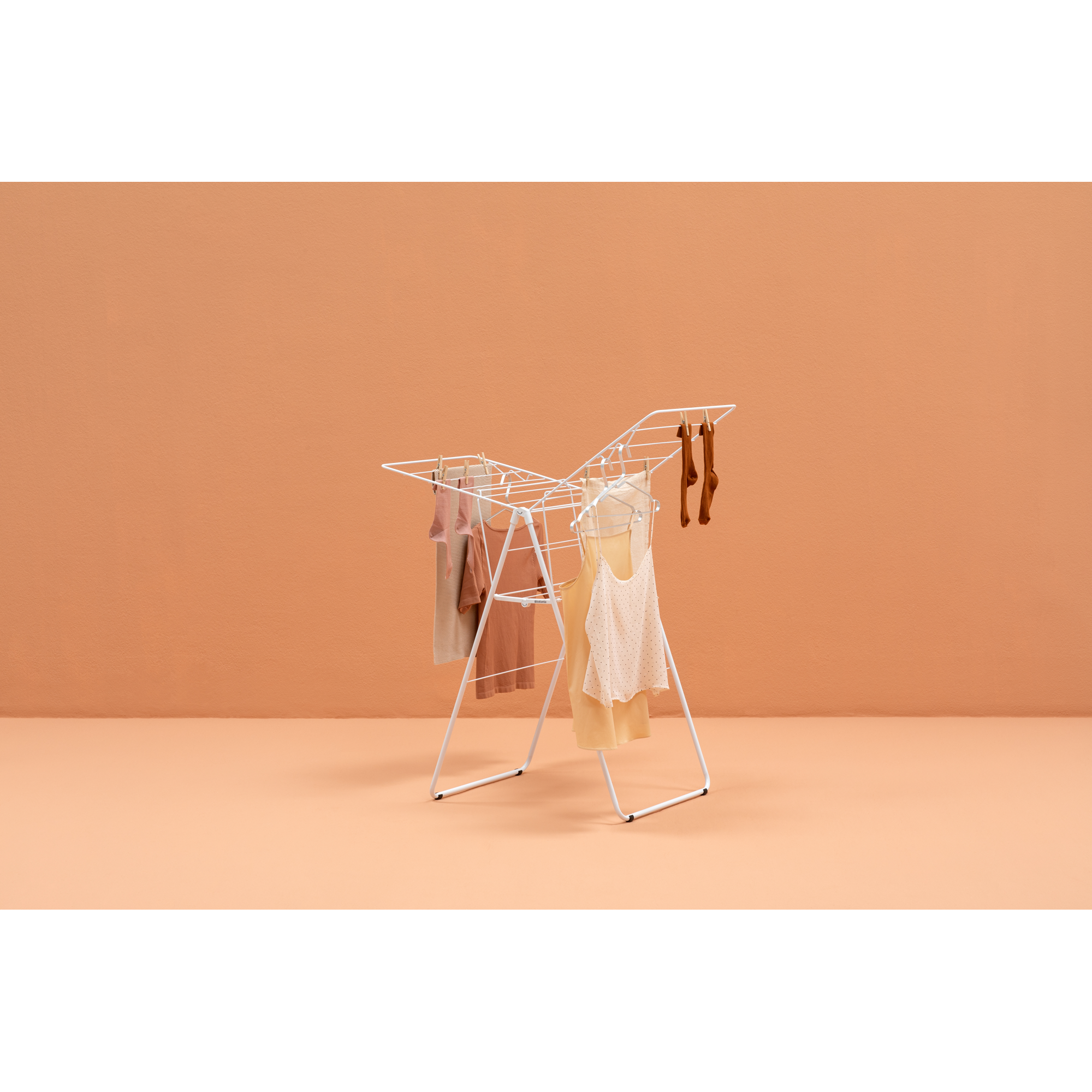 A white clothes drying rack with clothes and socks drying on an orange background.