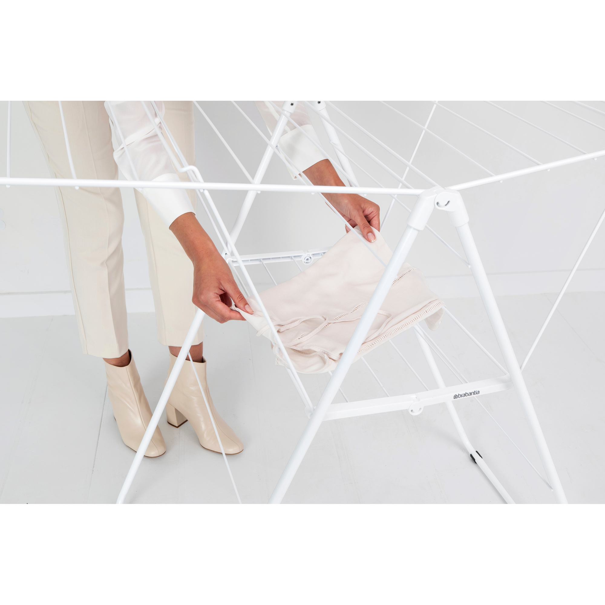 A person hangs a light-colored garment on a white drying rack.