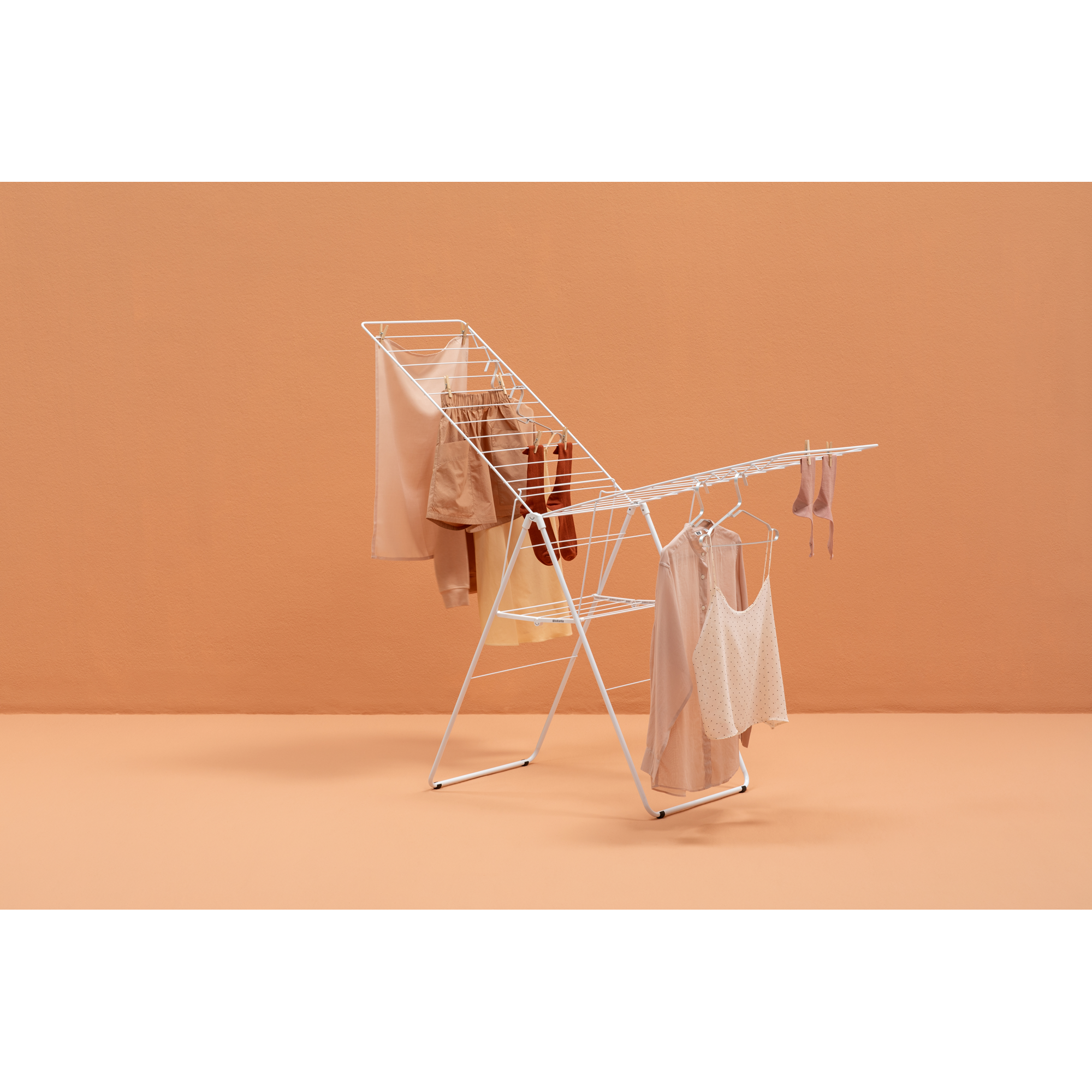 A white drying rack holds several light-colored clothes and socks against an orange background.