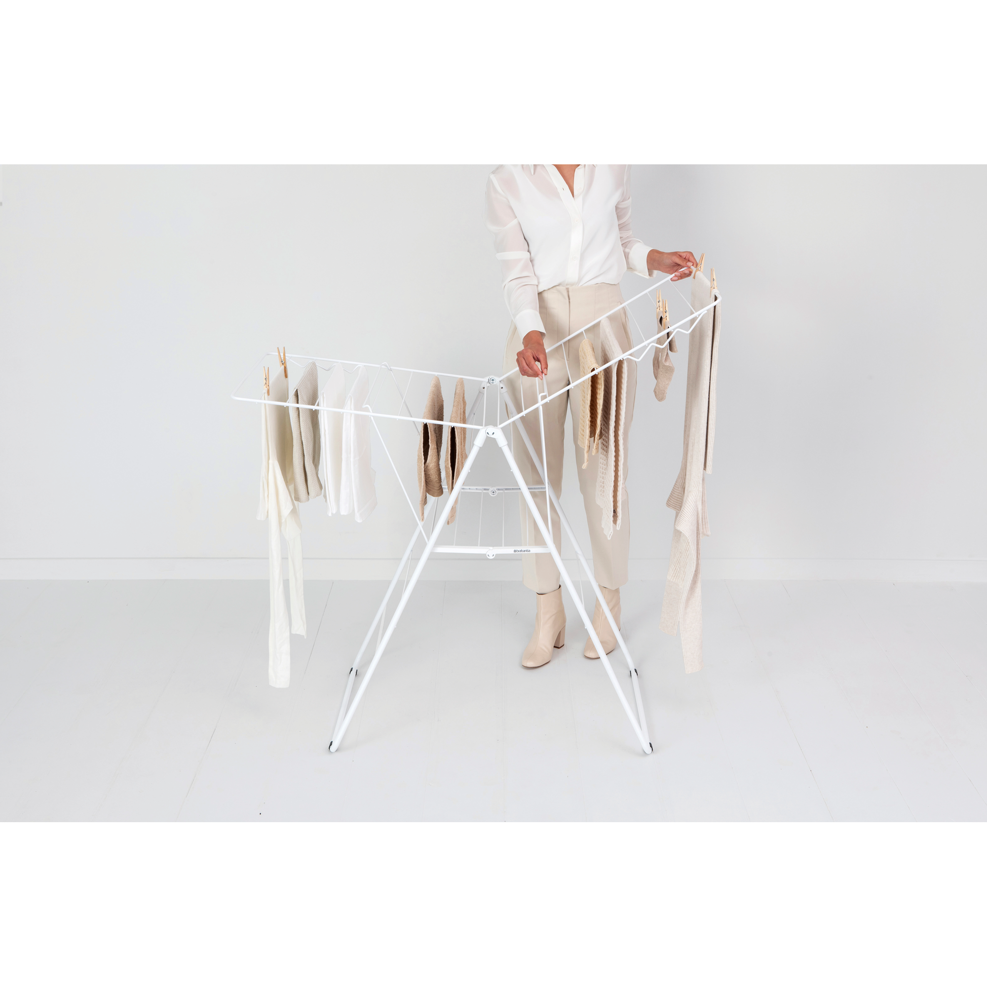 A woman hangs light-colored clothes on a white drying rack.