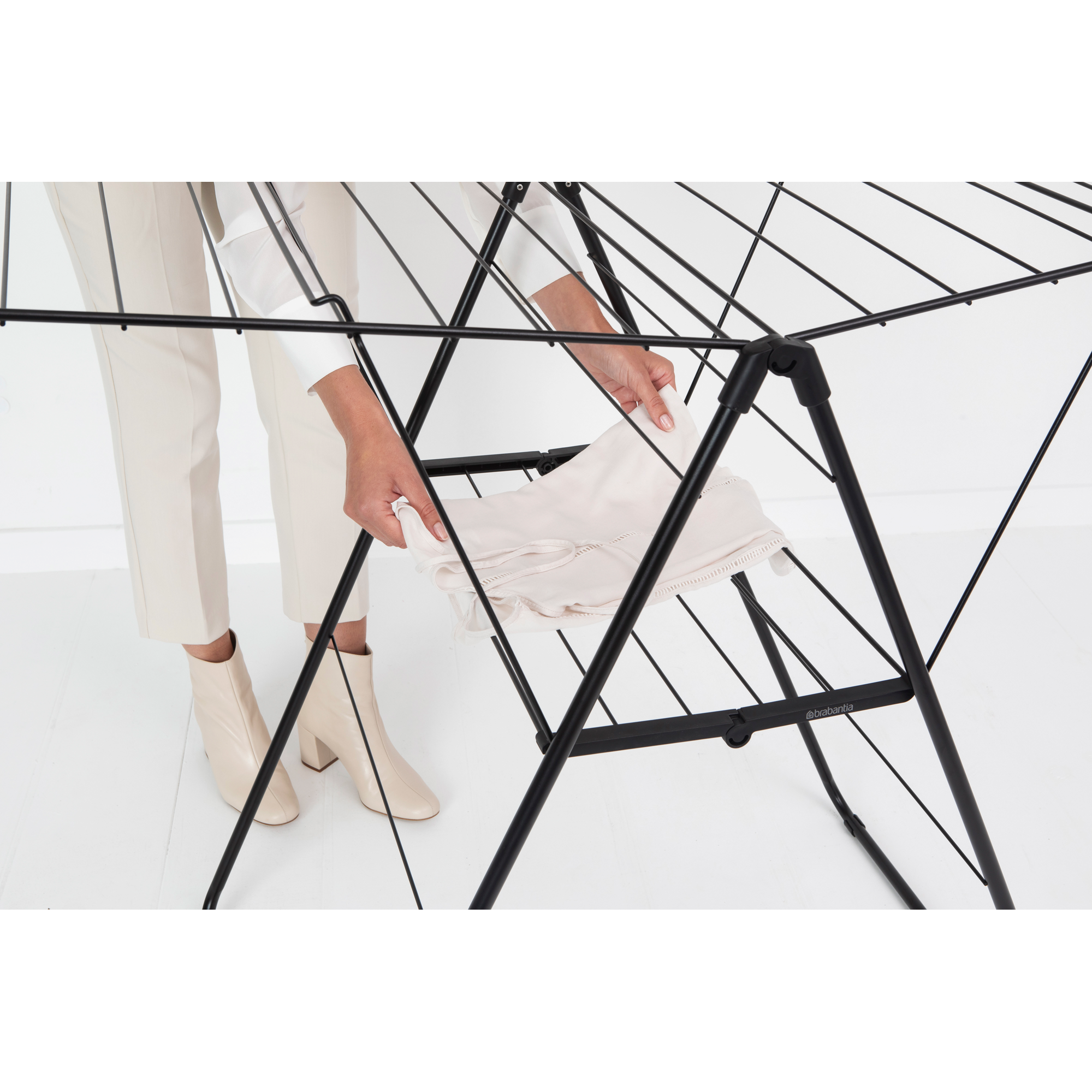 A person is folding a white cloth on a black drying rack.