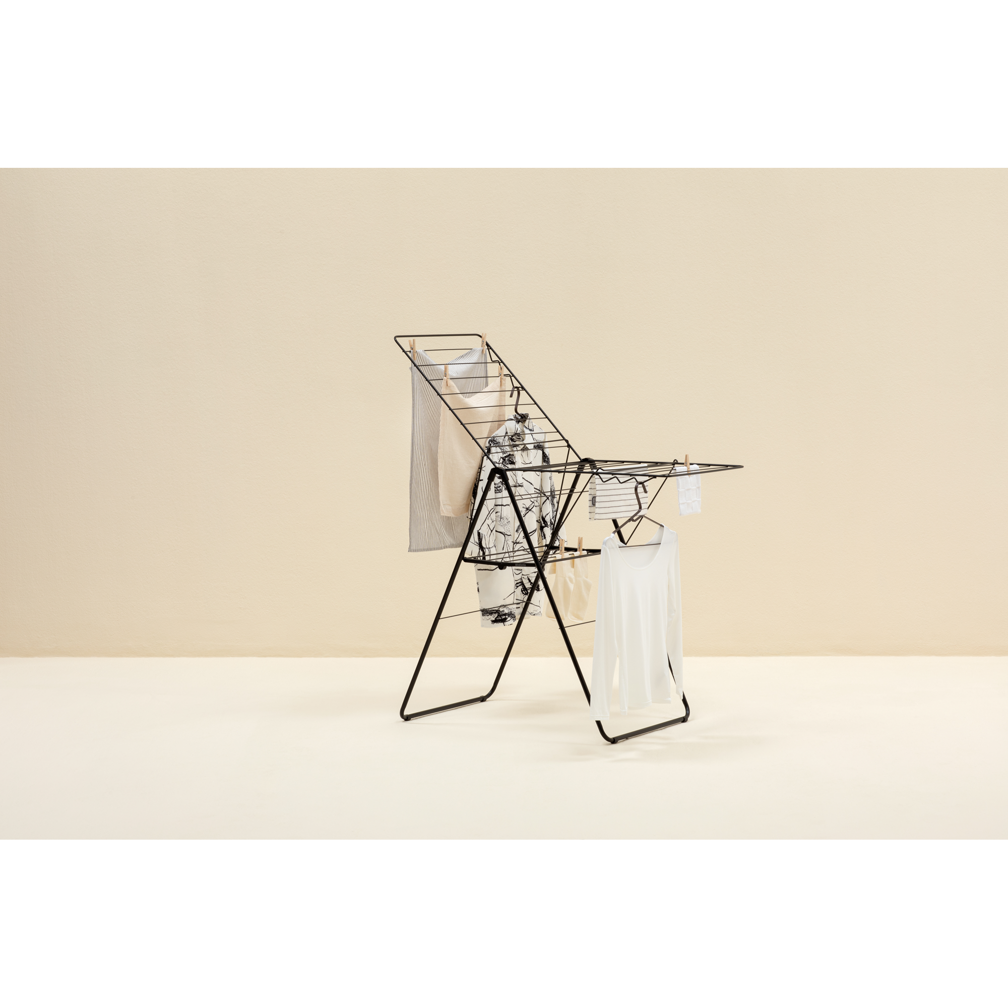 A black drying rack with clothes, including a white long-sleeved shirt.