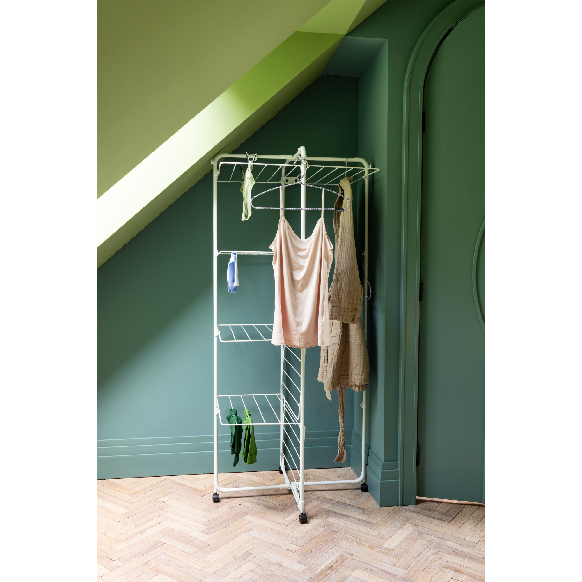 Een wit wasrek met kleding staat op een houten vloer.