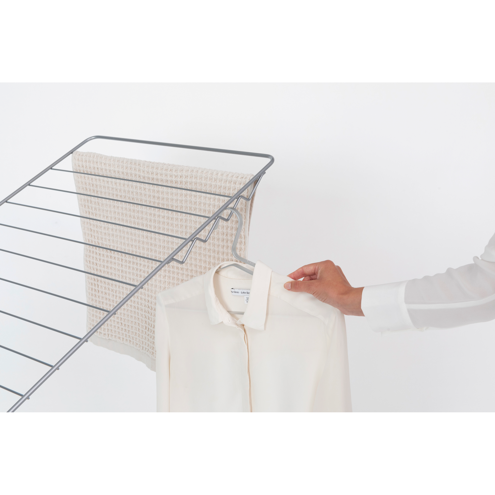 A hand hangs a cream-colored shirt on a hanger on a drying rack.