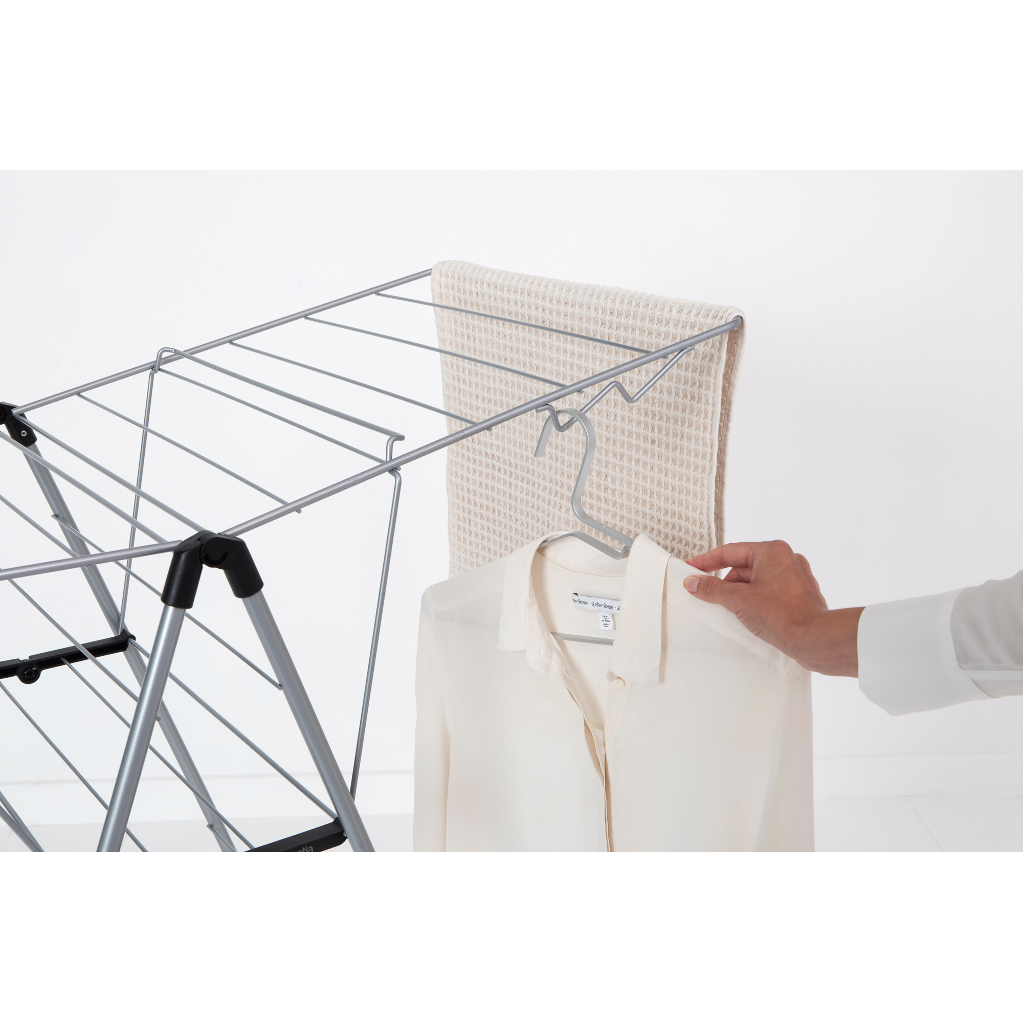 A hand hangs a cream-colored shirt on a drying rack next to a towel.