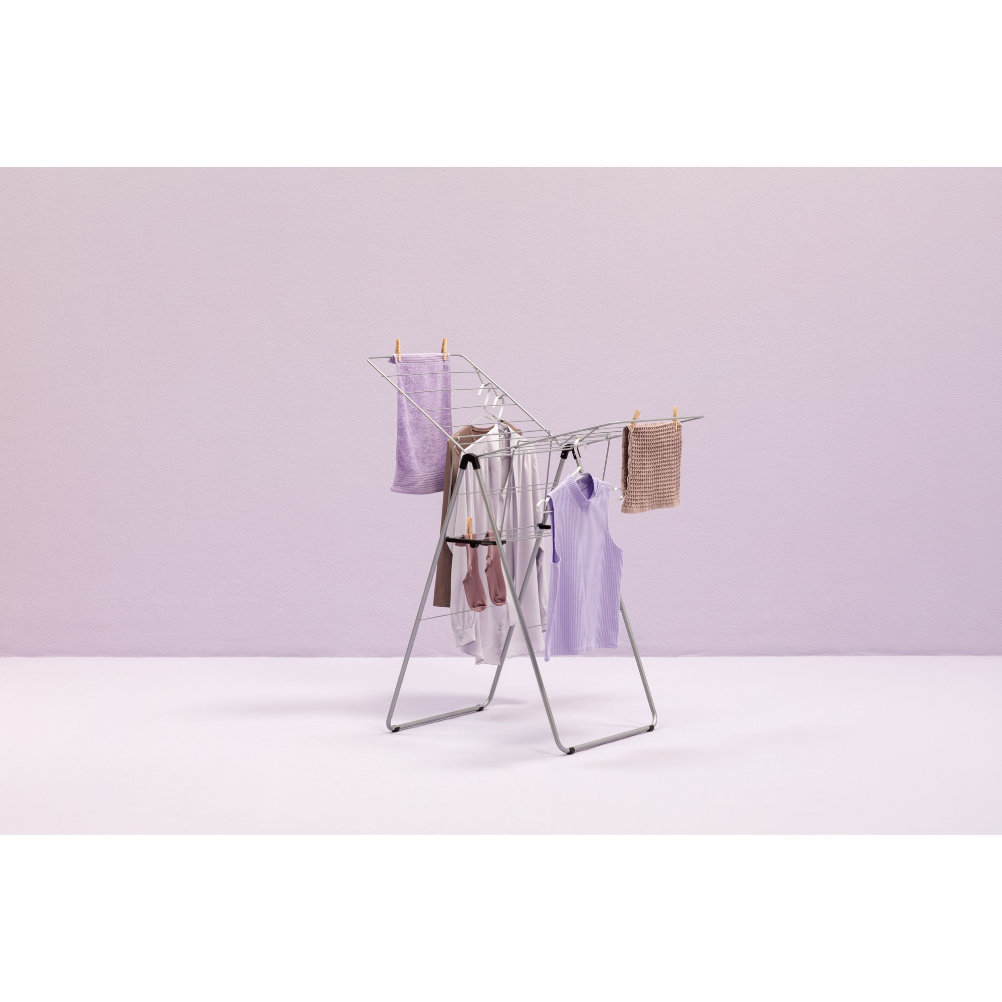 A drying rack with clothes and towels in front of a purple wall. Minimalist setup.