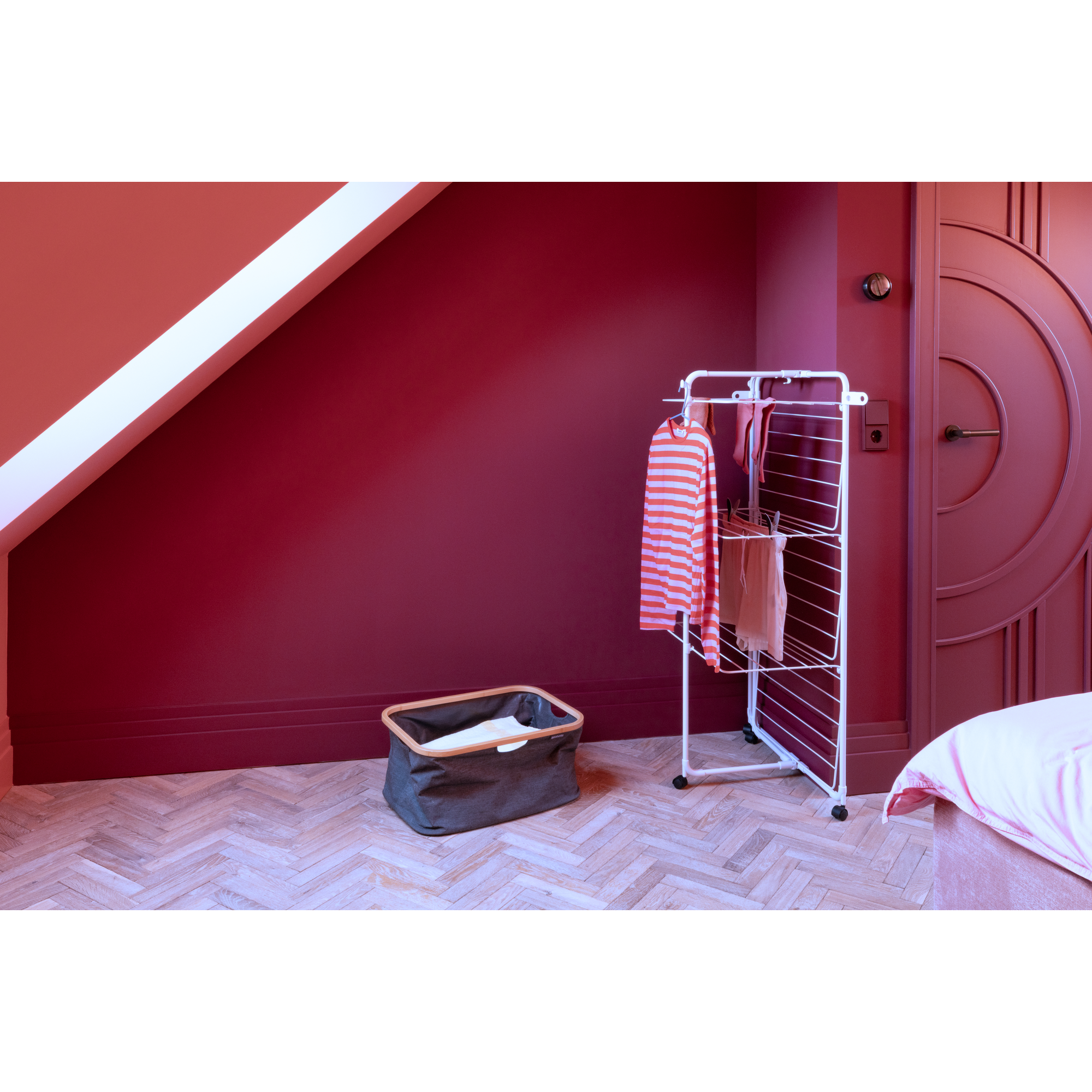 A drying rack with a striped shirt and laundry basket on a parquet floor.