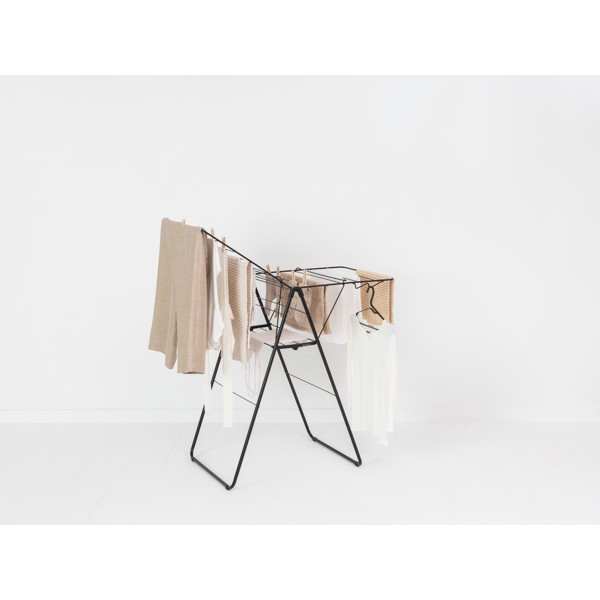 A black drying rack with beige and white clothes clipped on.