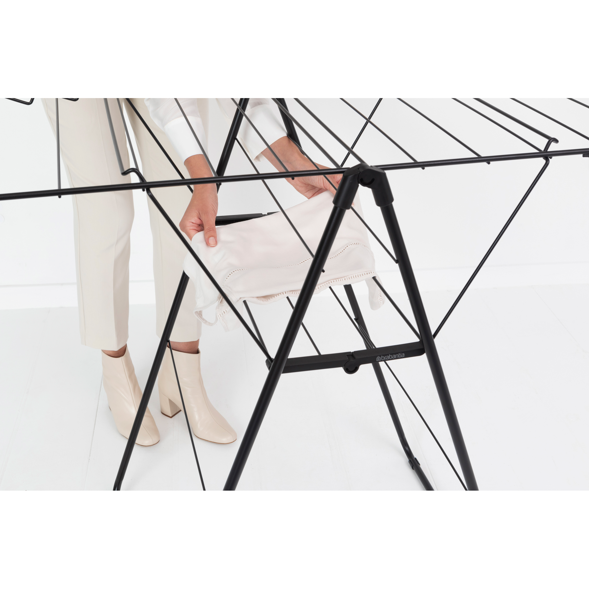 A person places white laundry on a black drying rack.