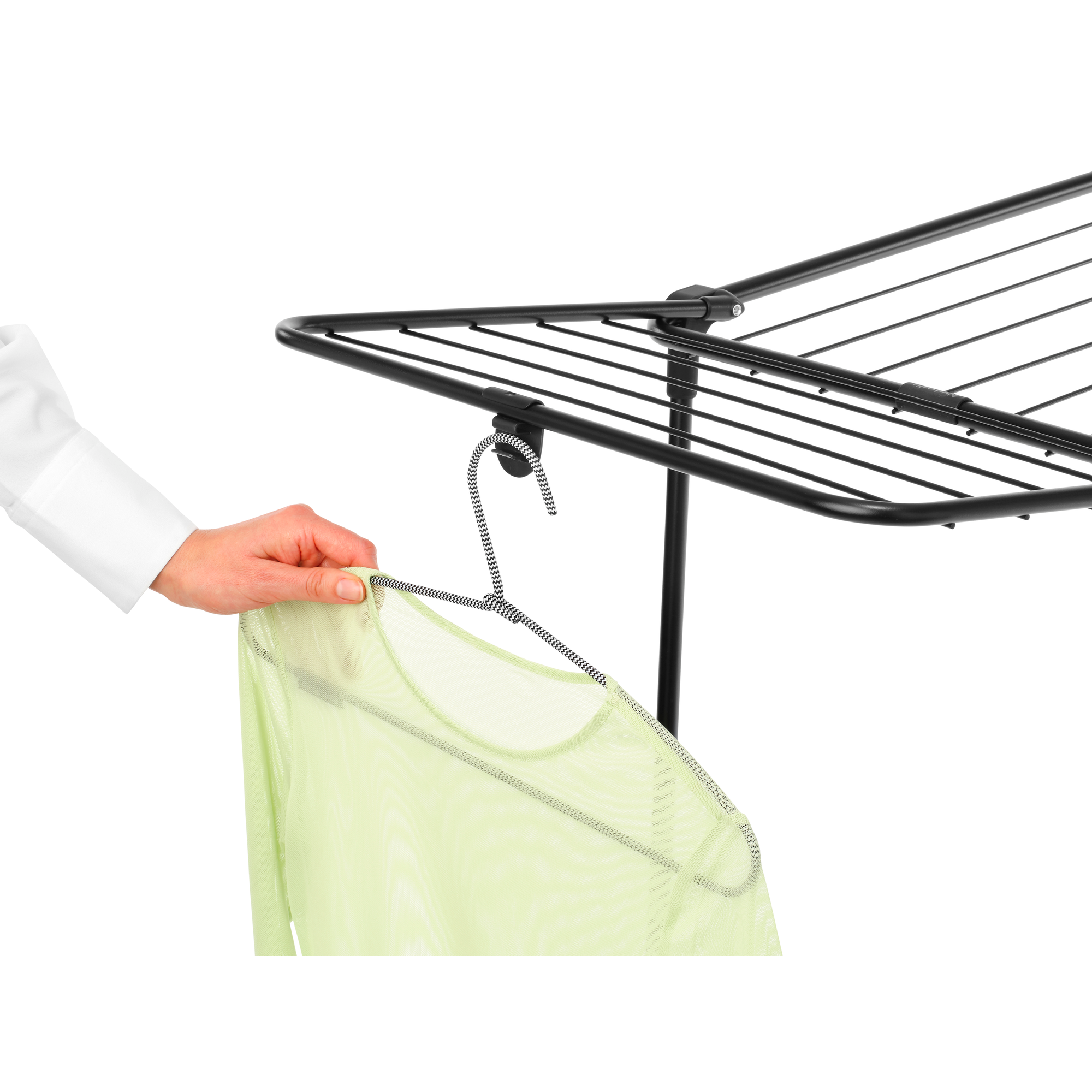 A hand hangs a light green shirt on a black and white hanger on a drying rack.