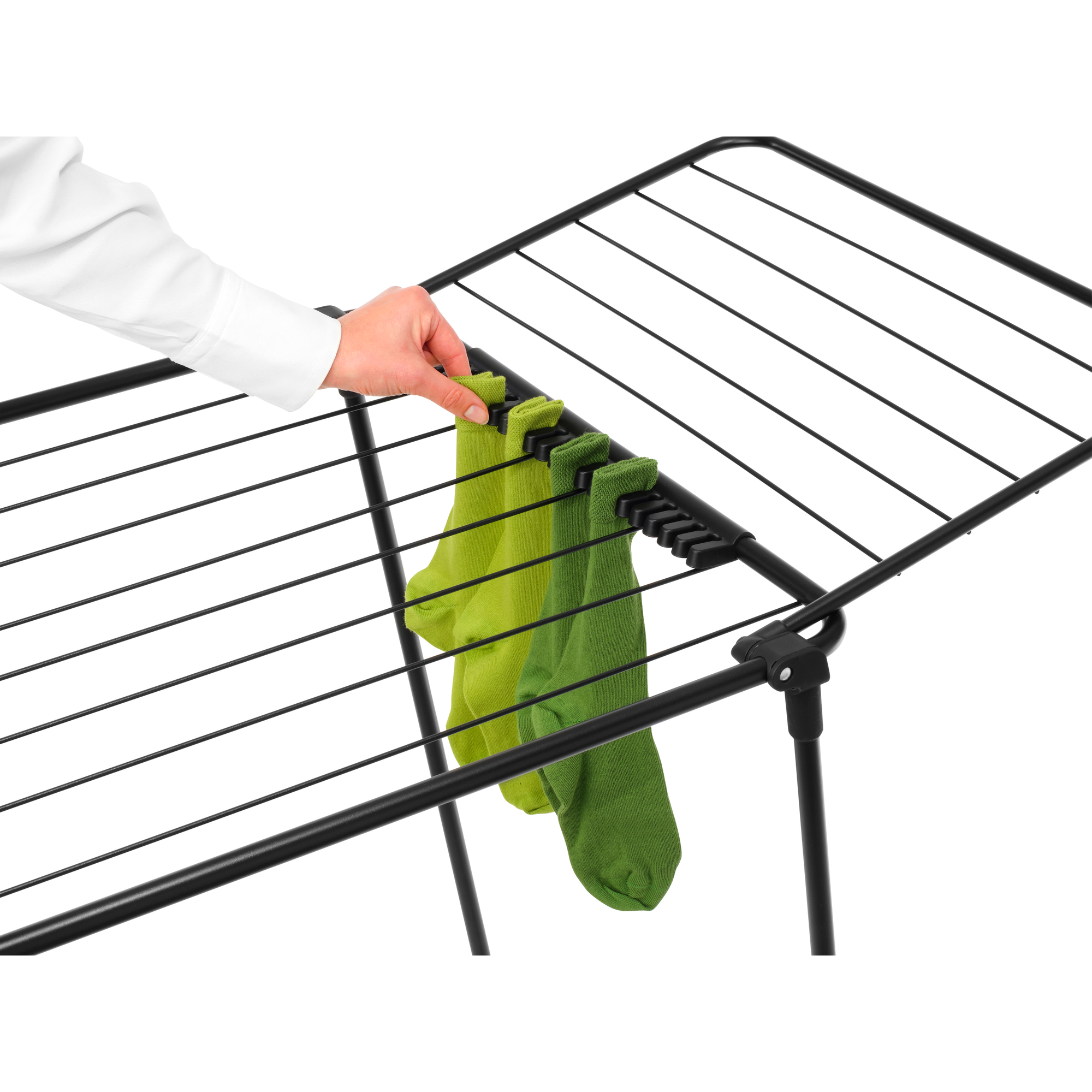 A hand in a white shirt hangs green socks on a black drying rack.
