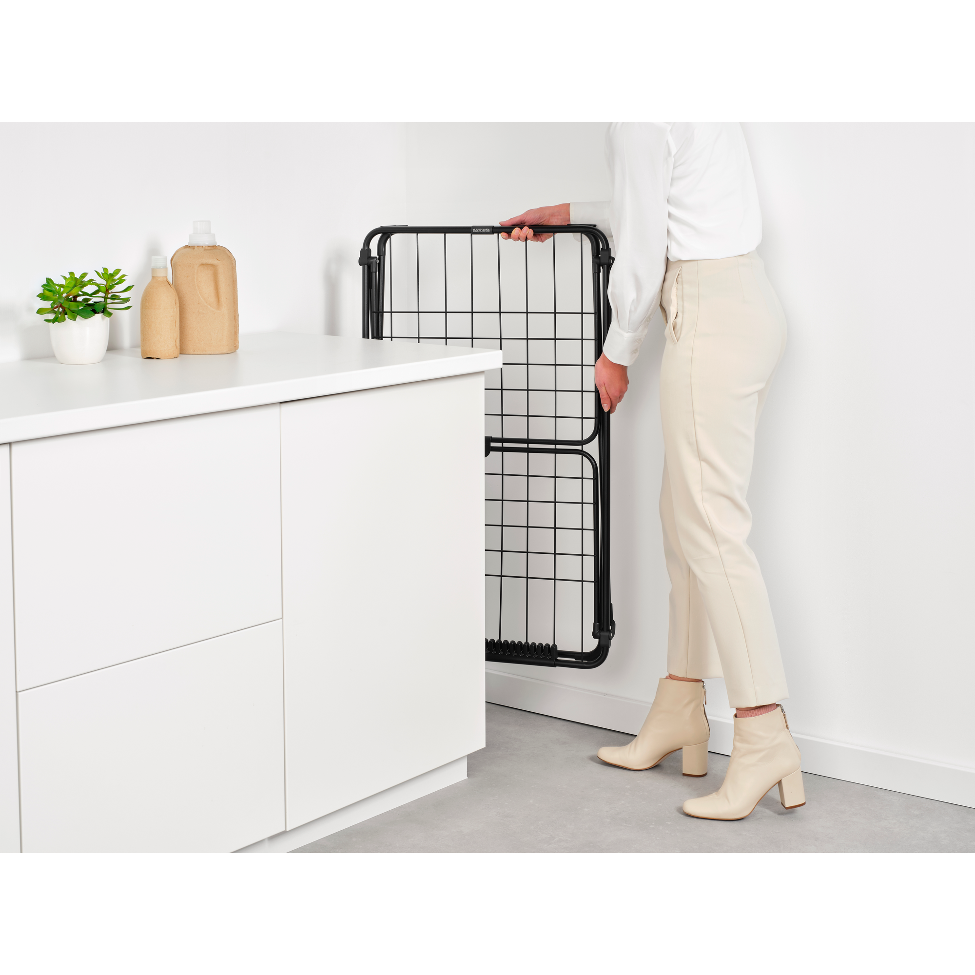 A person holds a black drying rack grid against a white wall.